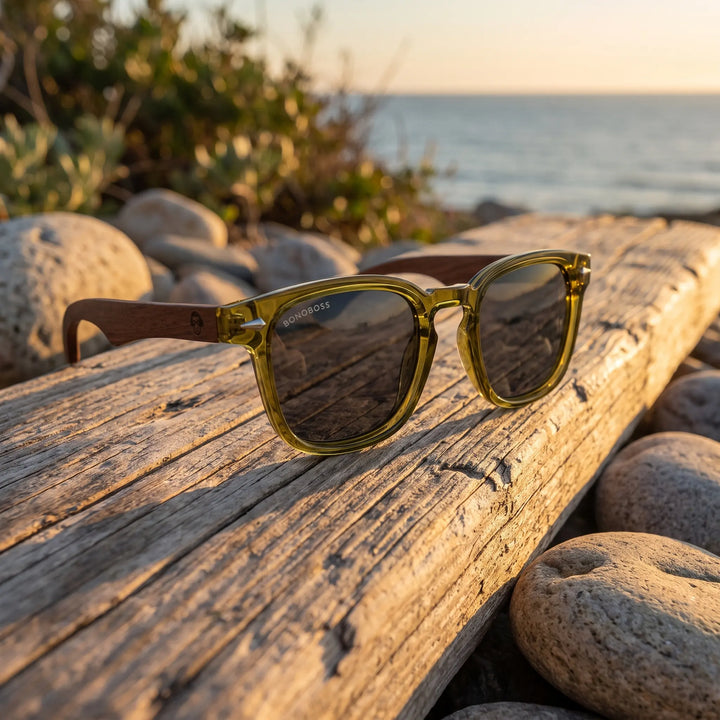Lentes de sol Bonoboss Creta Olive sobre madera y rocas junto al mar al atardecer #editorial_grid2 #color_olive