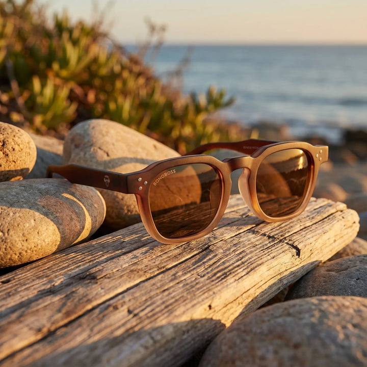 Lentes de sol Bonoboss Damero Brown sobre madera y rocas junto al mar al atardecer #editorial_grid2 #color_brown