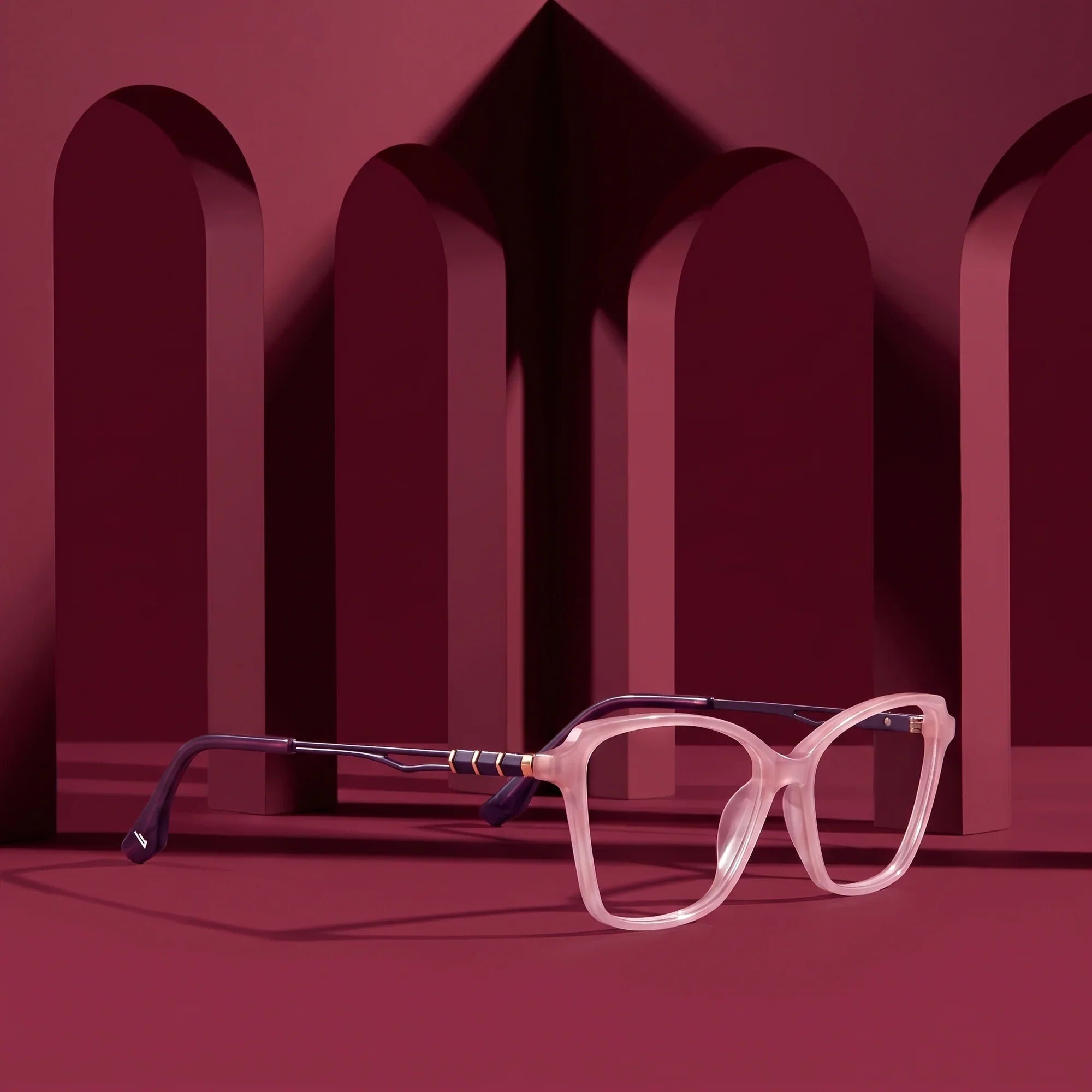 Anteojos Fiore 1006 en rosa – displayed on a burgundy podium among arches