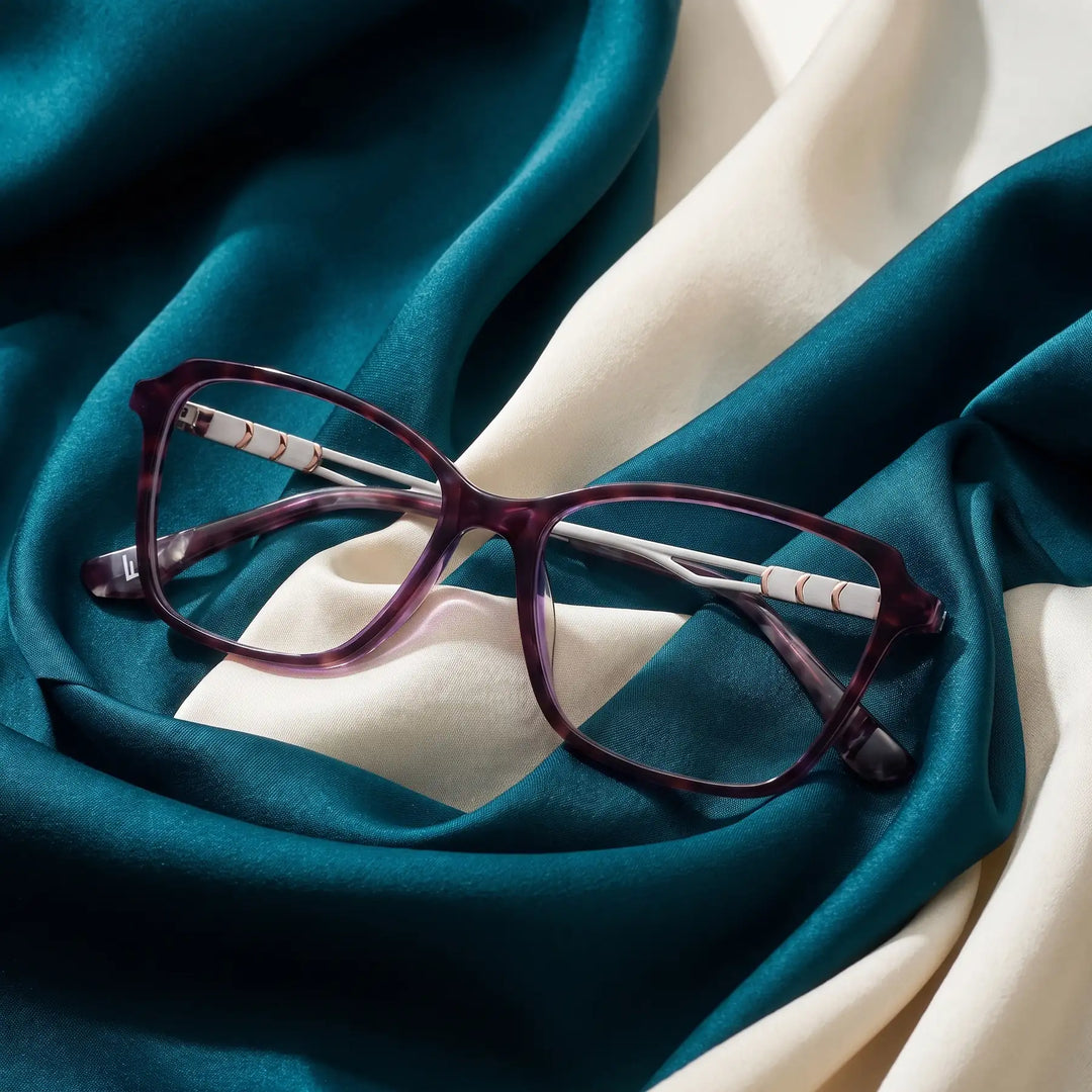 Anteojos Fiore 1006 en morado – resting on draped teal and ivory silk