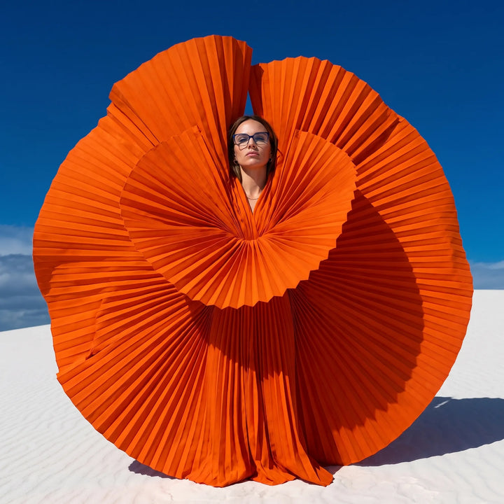 Anteojos Fiore 1006 en azul, en modelo – retrato de campaña, abanico plisado naranja escultórico sobre dunas blancas