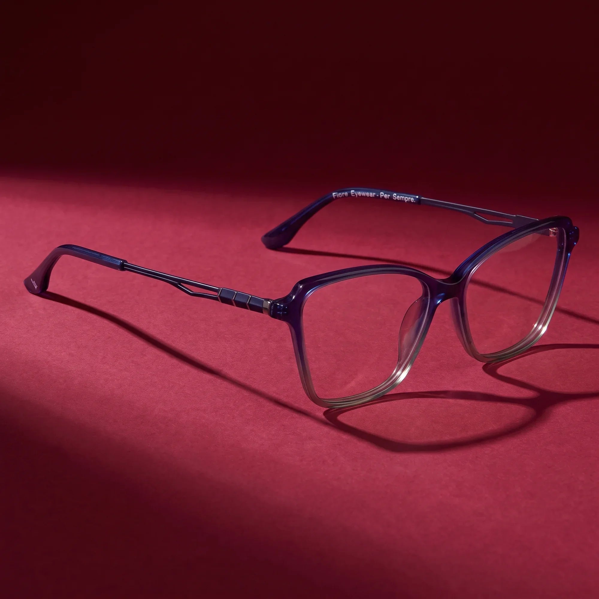 Anteojos Fiore 1006 en azul – editorial still life on a saturated burgundy set
