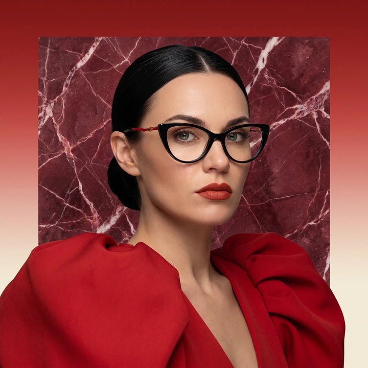 Anteojos Fiore 1010 en negro, en modelo – retrato de campaña, fondo de mármol rojo y vestido escarlata drapeado