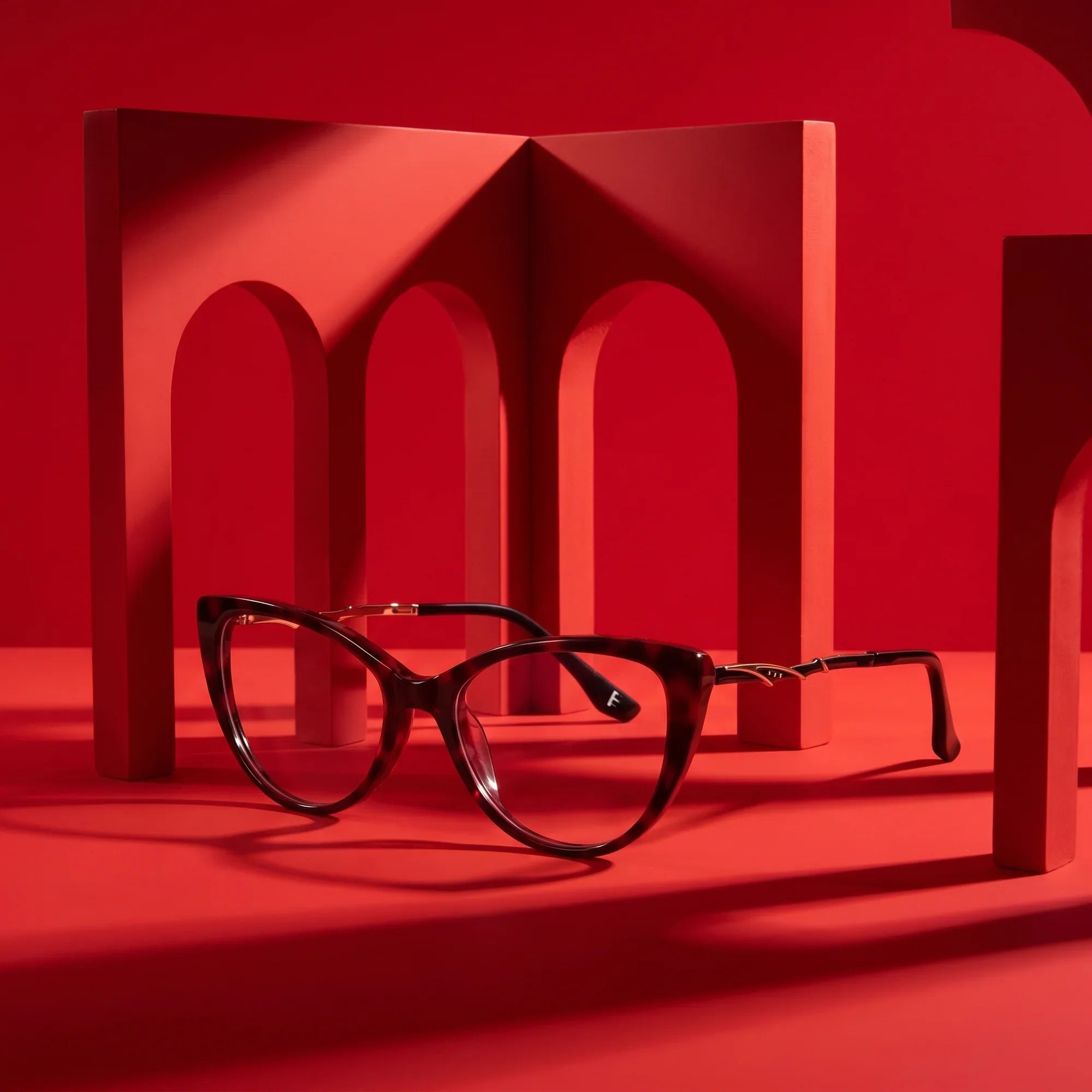 Anteojos Fiore 1010 en rojo – displayed on a vivid red podium among arches