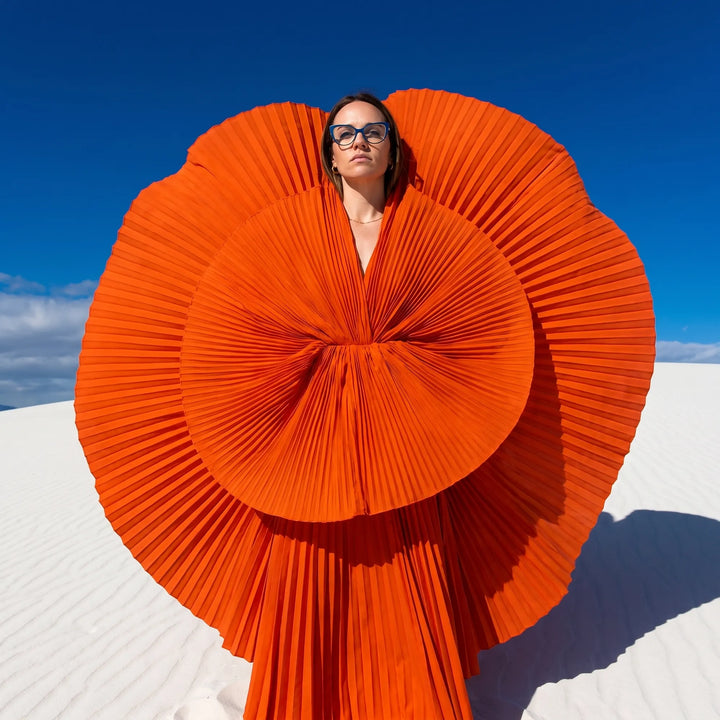 Anteojos Fiore 1010 en blue green, en modelo – retrato de campaña, abanico plisado naranja escultórico sobre dunas blancas