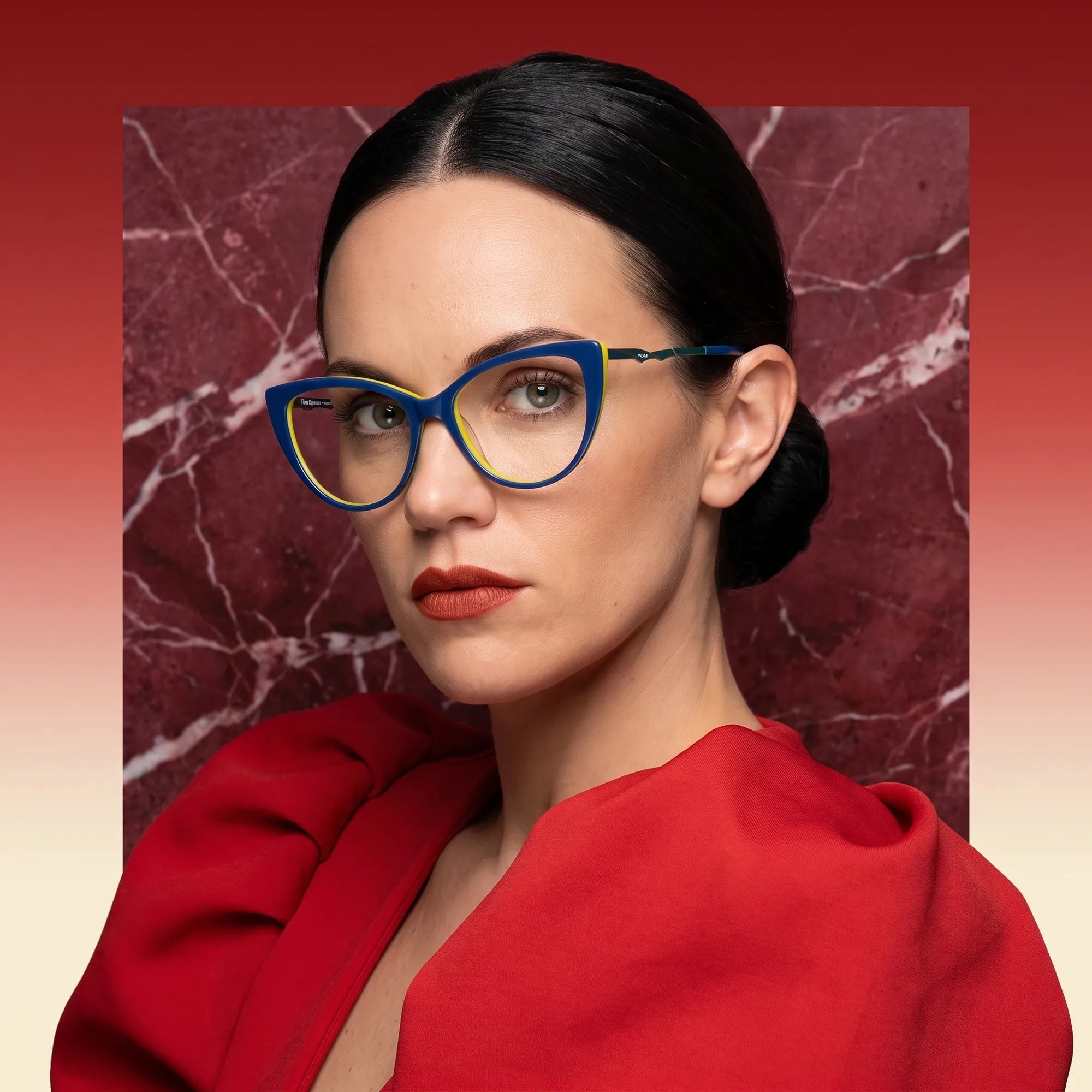 Anteojos Fiore 1010 en blue green, en modelo – retrato de campaña, fondo de mármol rojo y vestido escarlata drapeado