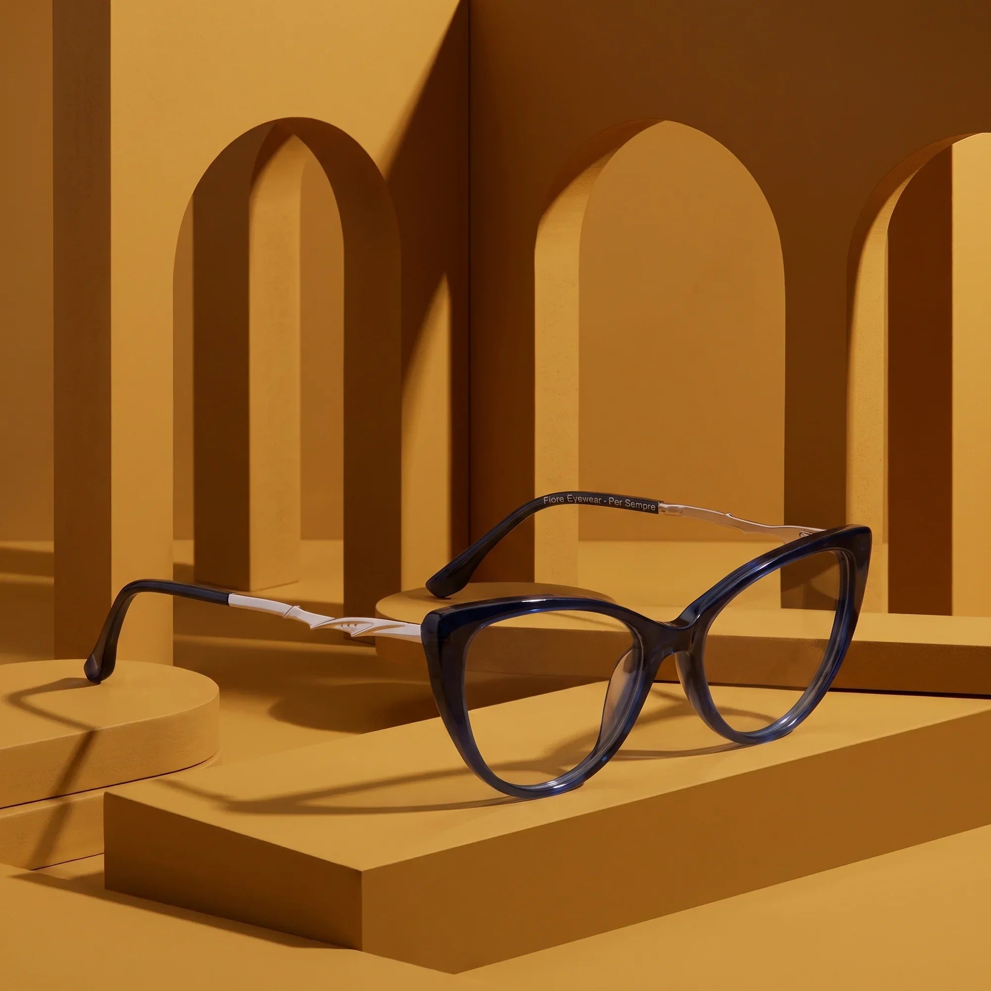 Anteojos Fiore 1010 en azul – displayed on a mustard ochre podium among arches