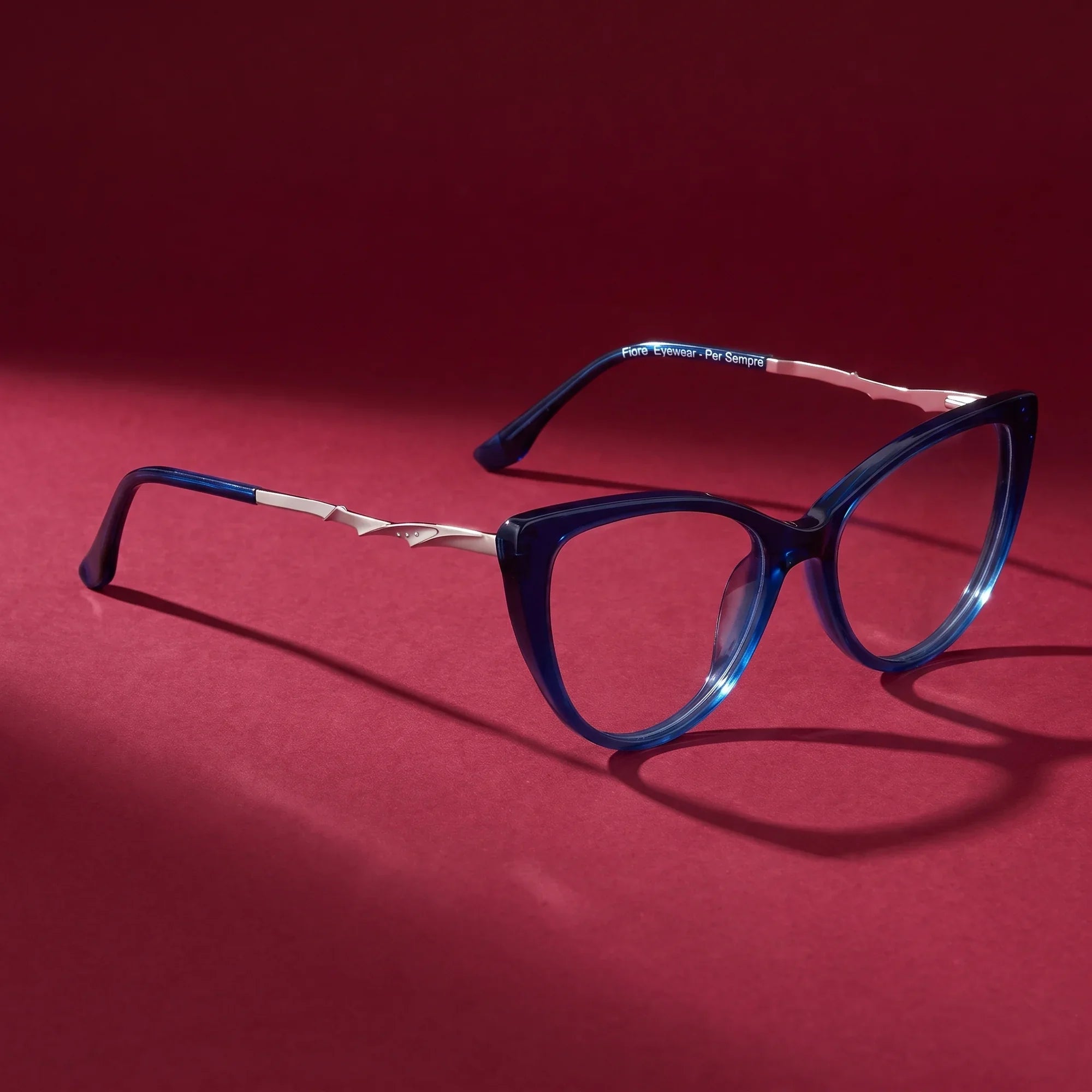 Anteojos Fiore 1010 en azul – editorial still life on a saturated burgundy set
