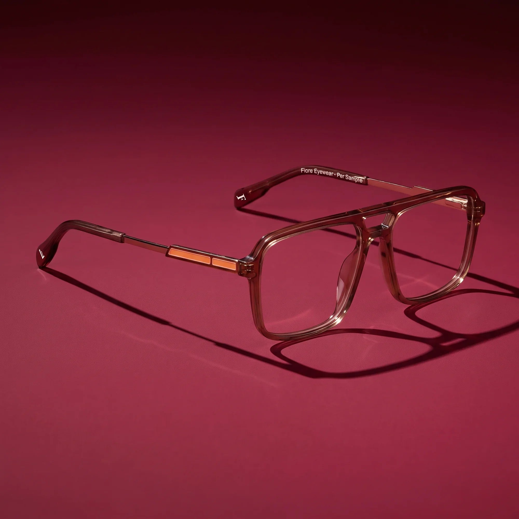 Anteojos Fiore 1014 en café – editorial still life on a saturated burgundy set