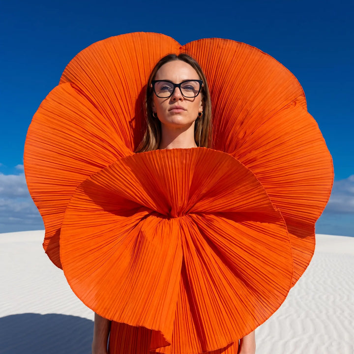 Anteojos Fiore 10172 en negro, en modelo – retrato de campaña, abanico plisado naranja escultórico sobre dunas blancas