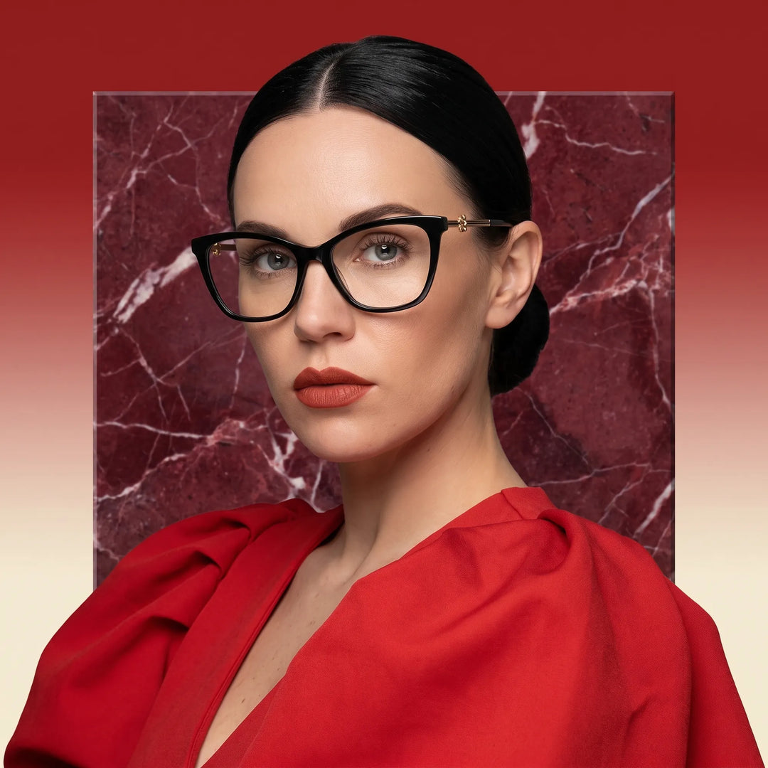 Anteojos Fiore 10172 en negro, en modelo – retrato de campaña, fondo de mármol rojo y vestido escarlata drapeado