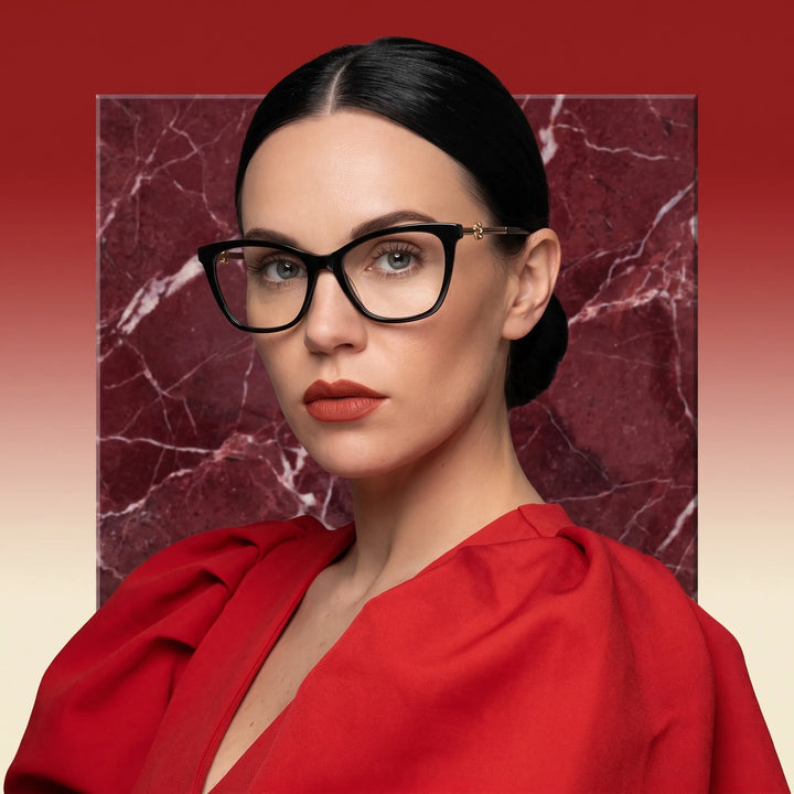 Anteojos Fiore 10172 en negro, en modelo – retrato de campaña, fondo de mármol rojo y vestido escarlata drapeado