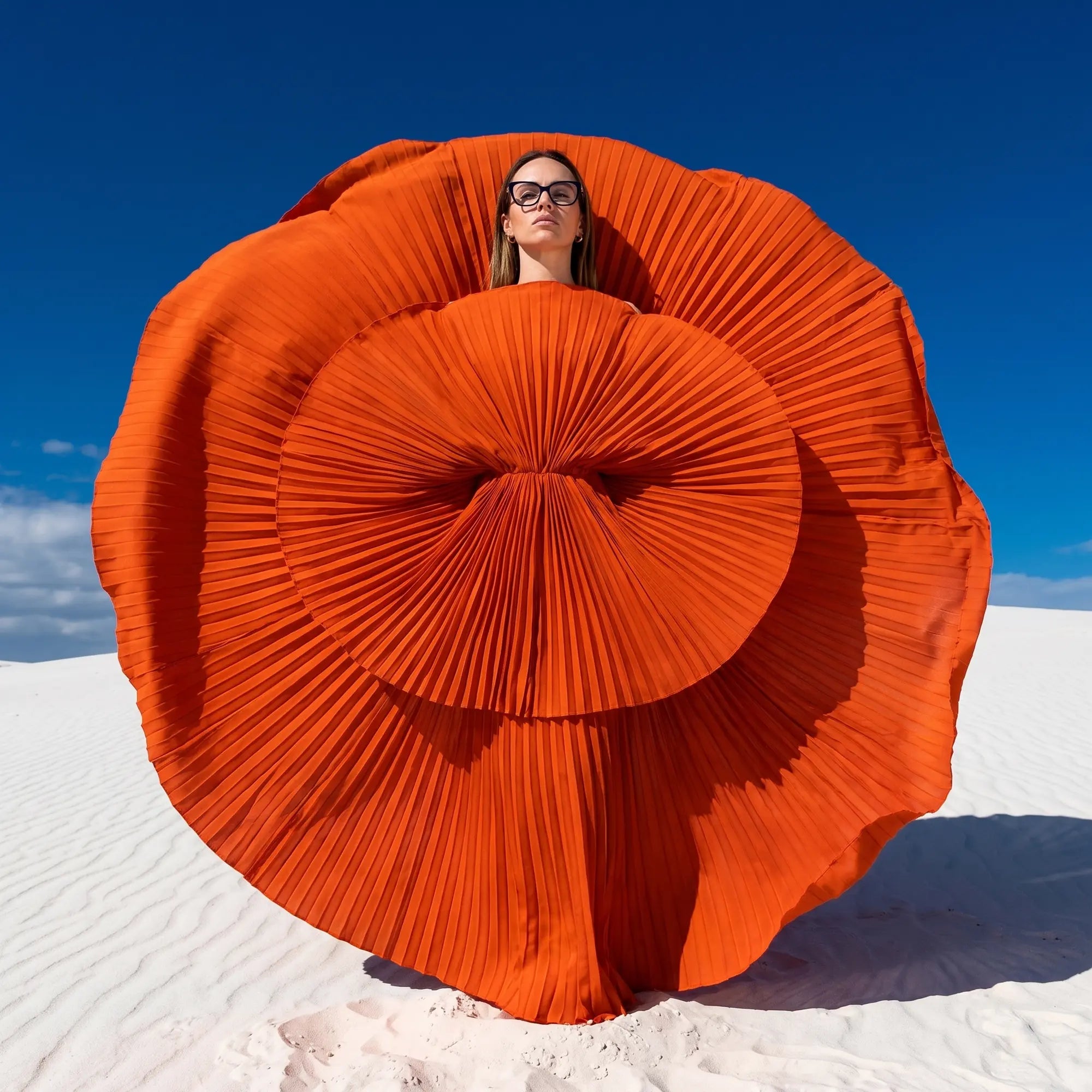 Anteojos Fiore 10172 en azul, en modelo – retrato de campaña, abanico plisado naranja escultórico sobre dunas blancas