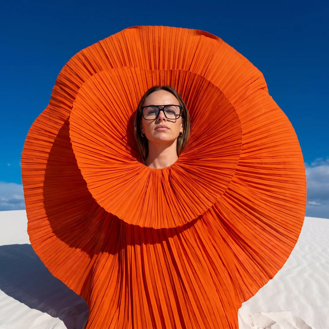Anteojos Fiore 10177 en negro, en modelo – retrato de campaña, abanico plisado naranja escultórico sobre dunas blancas