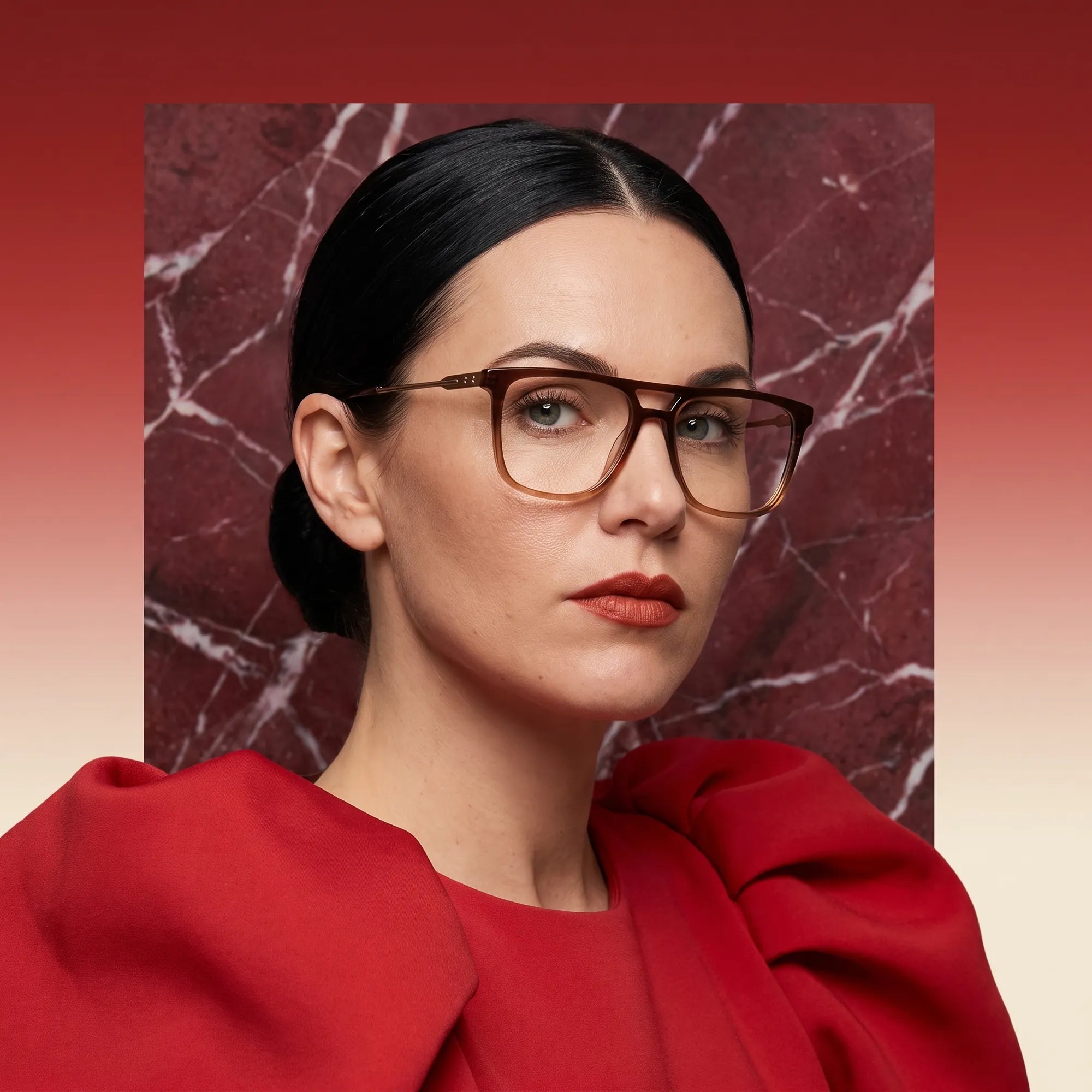Anteojos Fiore 10177 en café, en modelo – retrato de campaña, fondo de mármol rojo y vestido escarlata drapeado