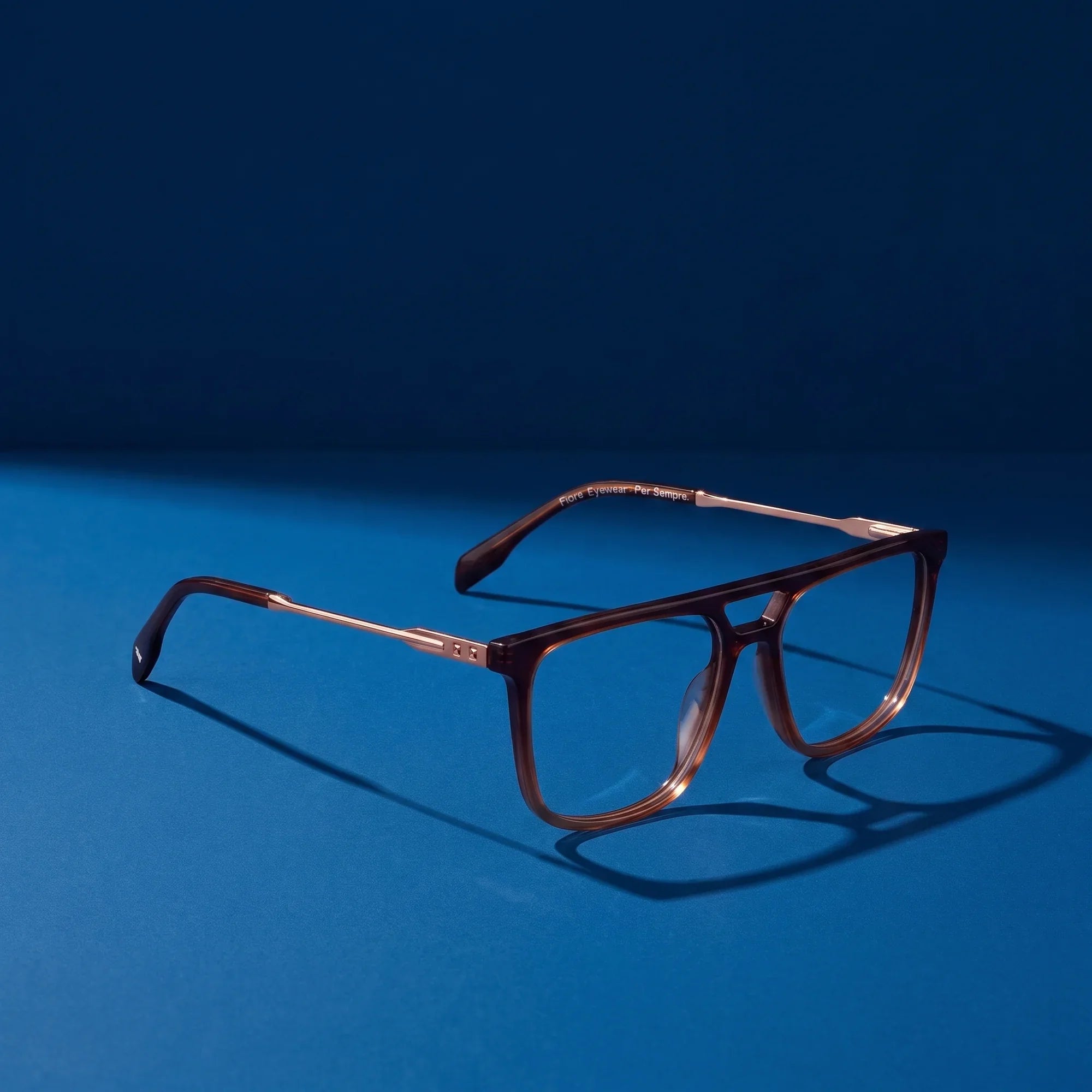 Anteojos Fiore 10177 en café – hero still life against a deep midnight blue backdrop