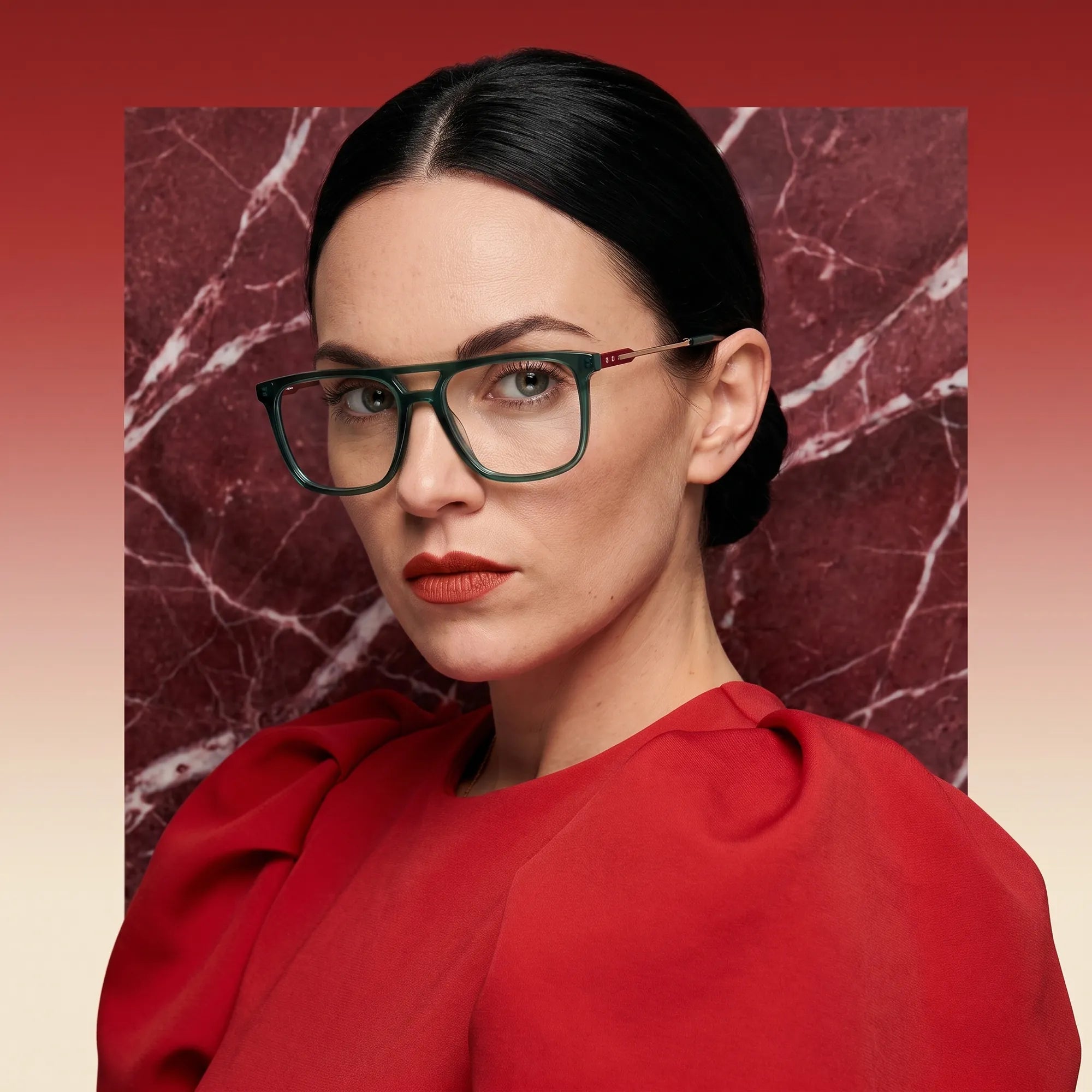 Anteojos Fiore 10177 en verde, en modelo – retrato de campaña, fondo de mármol rojo y vestido escarlata drapeado