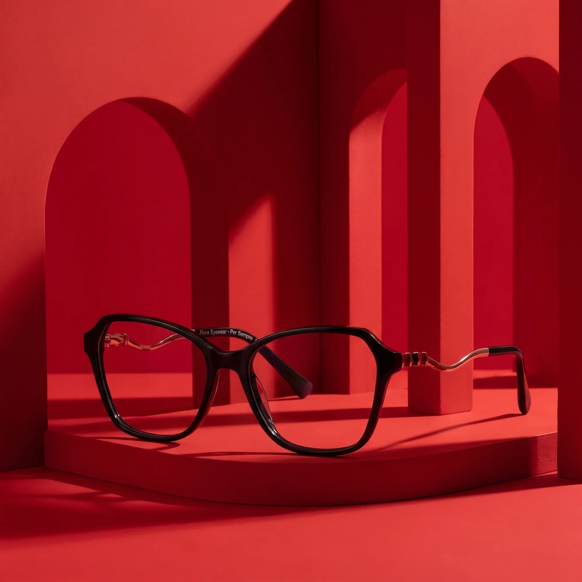 Anteojos Fiore 1030 en negro – staged on a sculptural vivid red architecture set