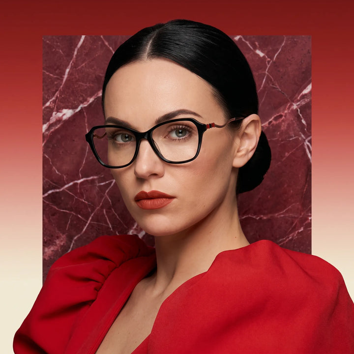 Anteojos Fiore 1030 en negro, en modelo – retrato de campaña, fondo de mármol rojo y vestido escarlata drapeado