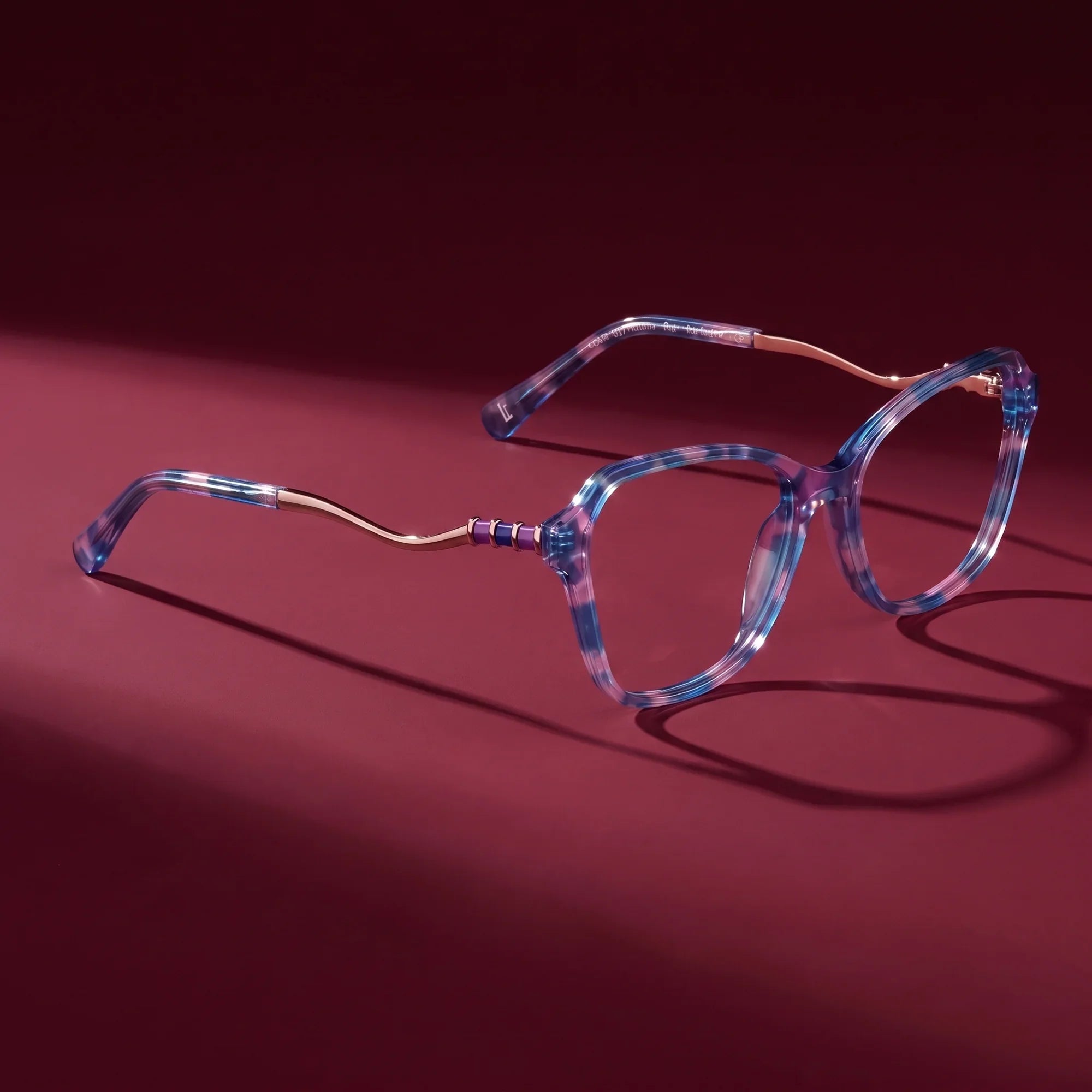Anteojos Fiore 1030 en blue pink – hero still life against a deep burgundy backdrop