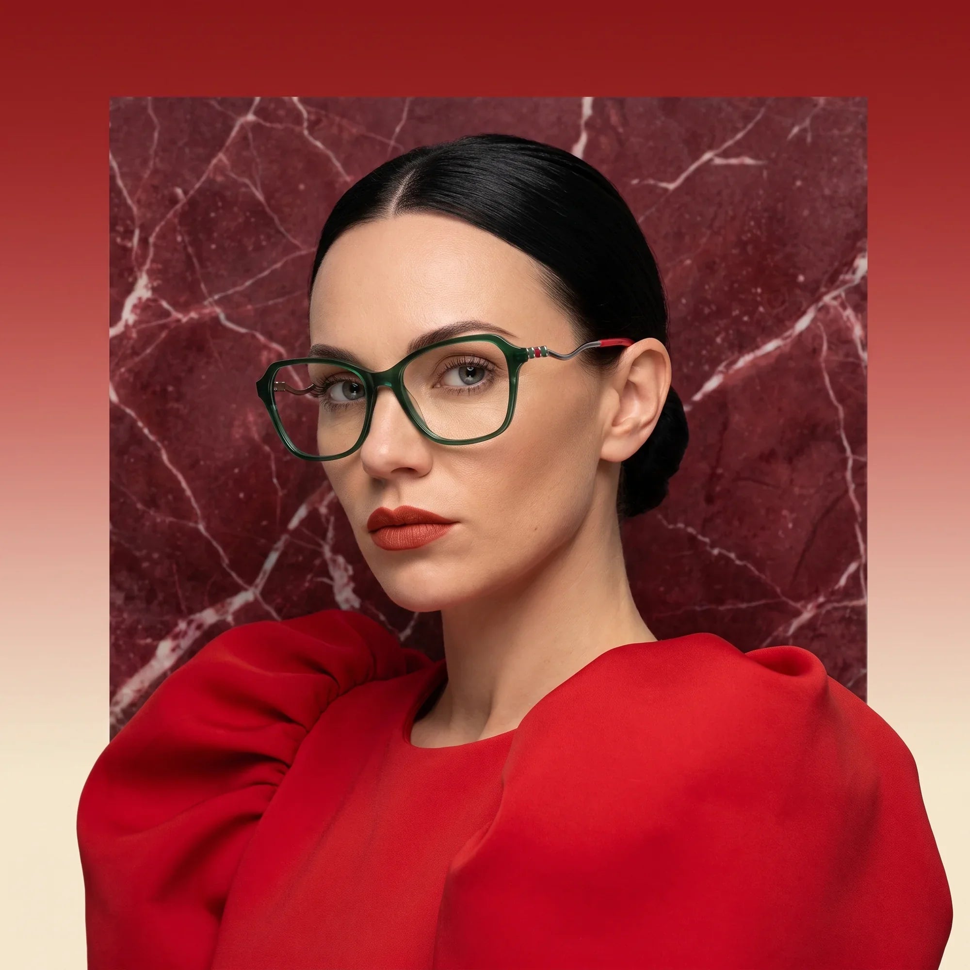 Anteojos Fiore 1030 en verde, en modelo – retrato de campaña, fondo de mármol rojo y vestido escarlata drapeado