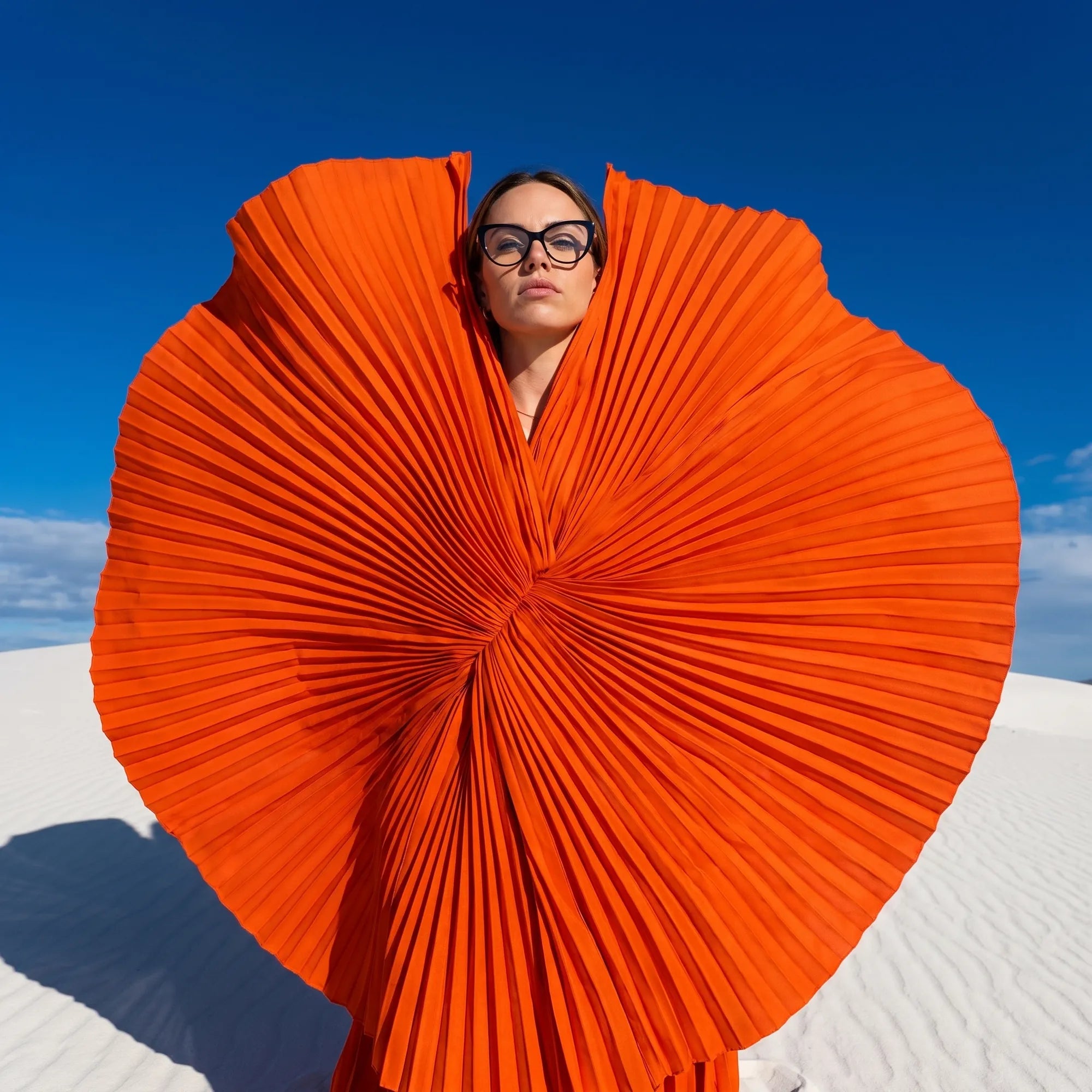 Anteojos Fiore 1031 en negro, en modelo – retrato de campaña, abanico plisado naranja escultórico sobre dunas blancas
