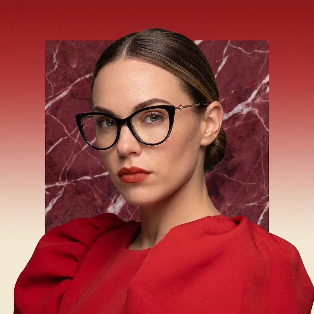 Anteojos Fiore 1031 en negro, en modelo – retrato de campaña, fondo de mármol rojo y vestido escarlata drapeado