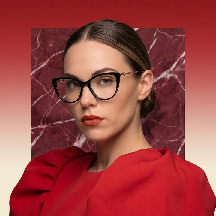 Anteojos Fiore 1031 en negro, en modelo – retrato de campaña, fondo de mármol rojo y vestido escarlata drapeado