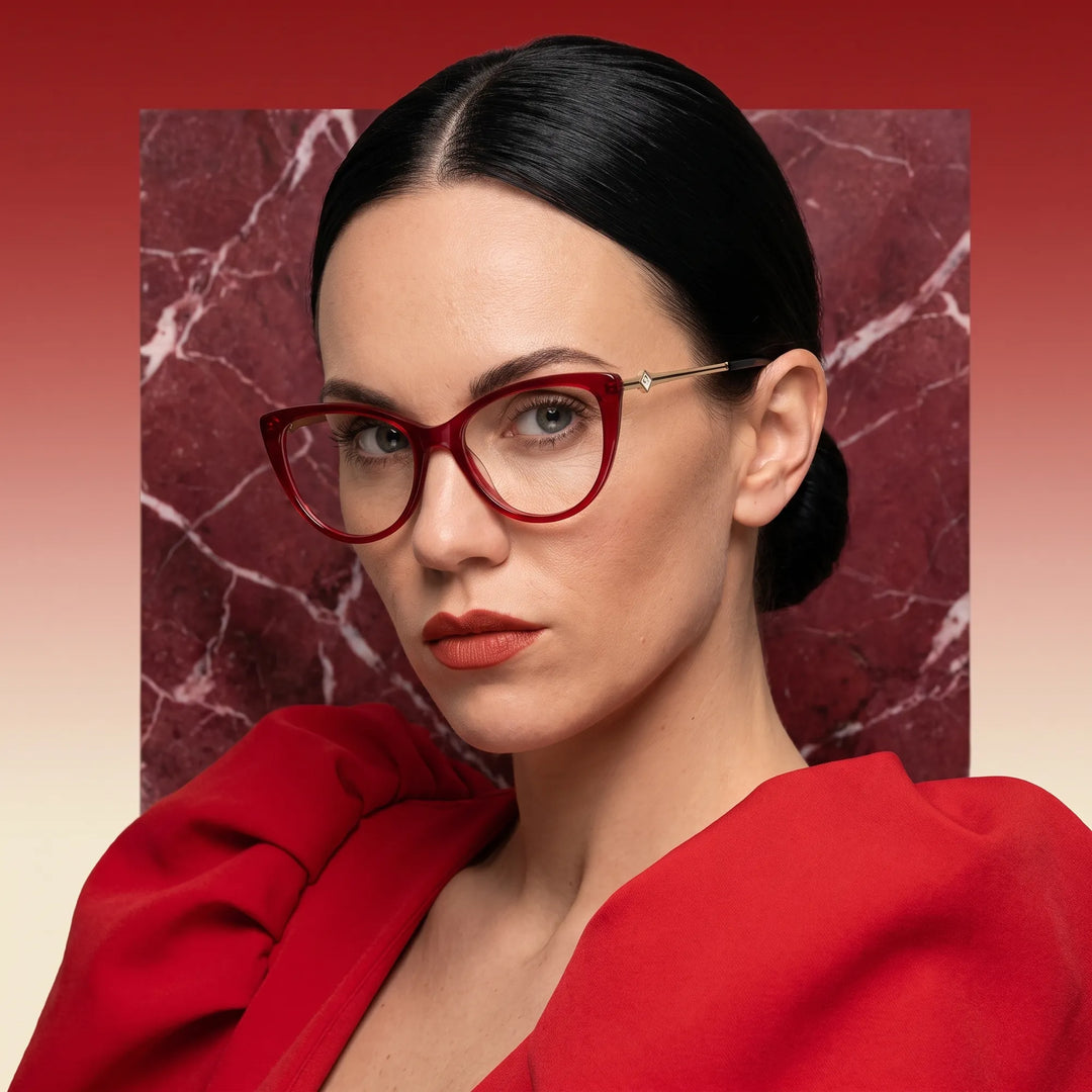 Anteojos Fiore 1031 en rojo, en modelo – retrato de campaña, fondo de mármol rojo y vestido escarlata drapeado