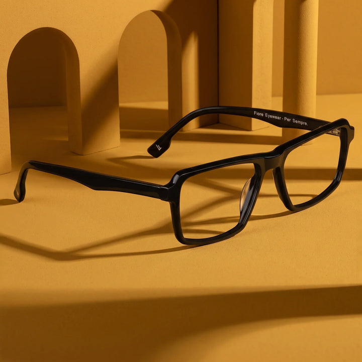 Anteojos Fiore 1038 en negro – displayed on a mustard ochre podium among arches