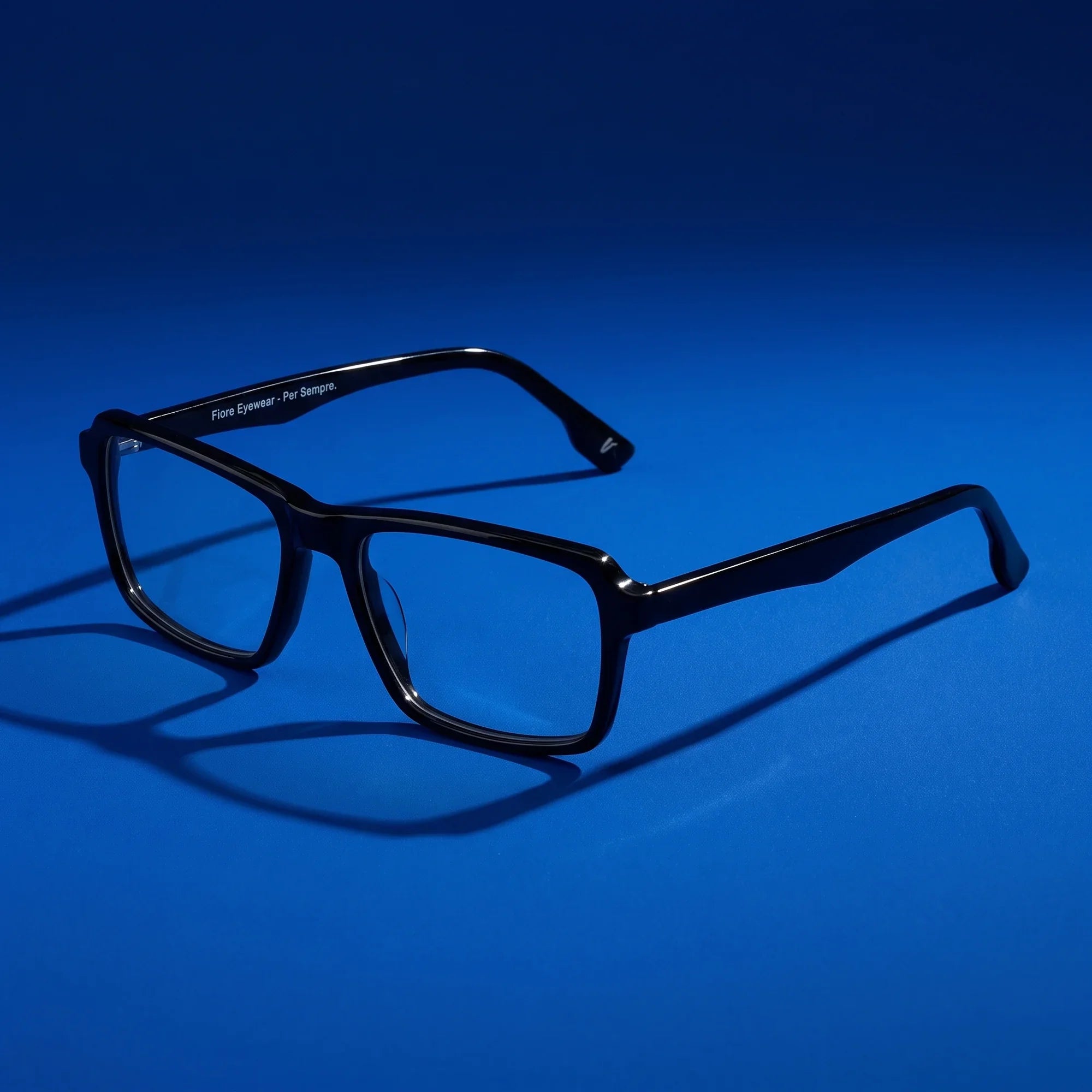 Anteojos Fiore 1038 en negro – hero still life against a deep cobalt backdrop
