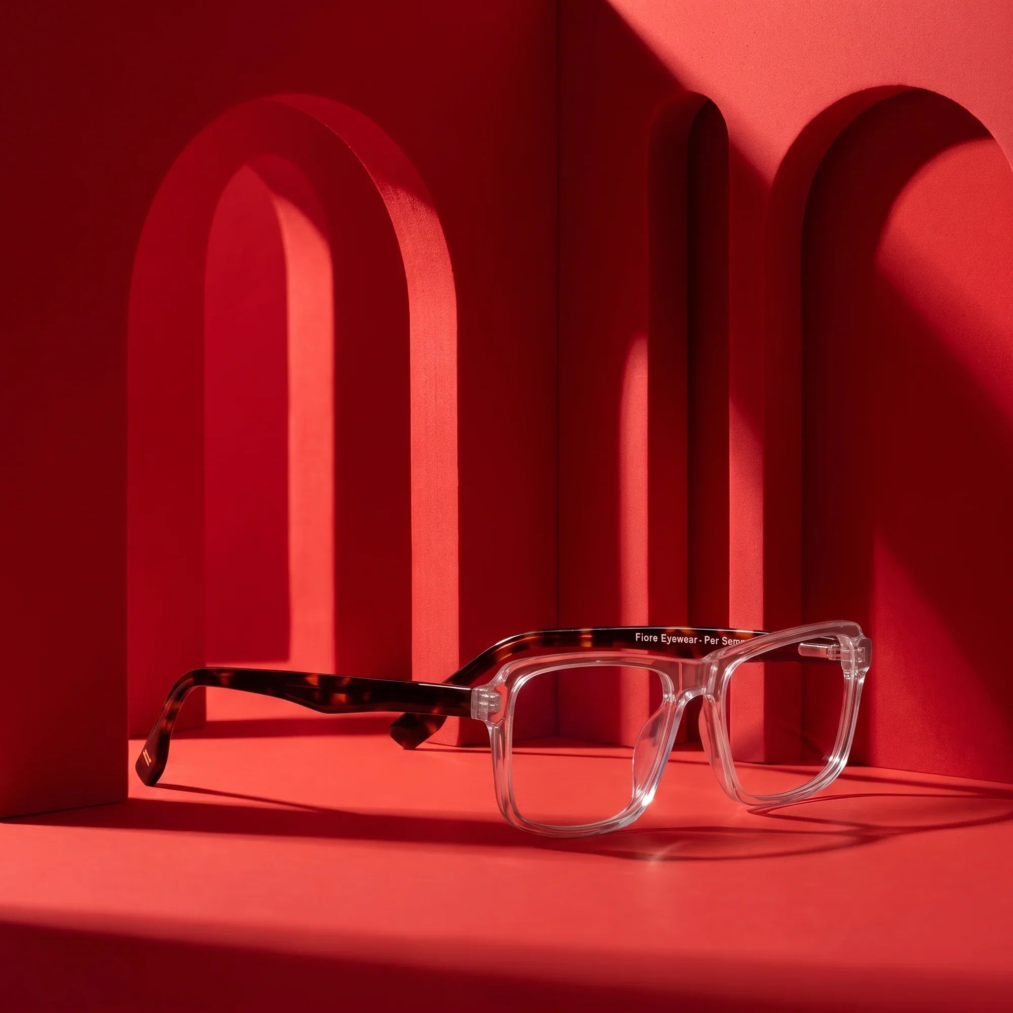 Anteojos Fiore 1038 en transparent – staged on a sculptural vivid red architecture set