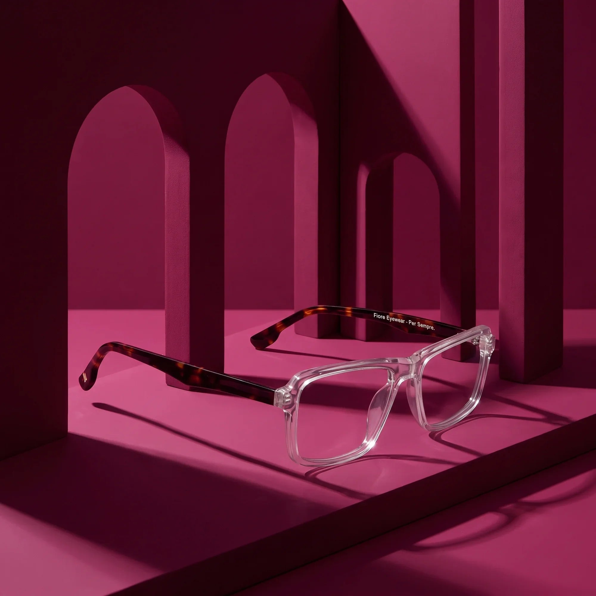 Anteojos Fiore 1038 en transparent – displayed on a magenta podium among arches