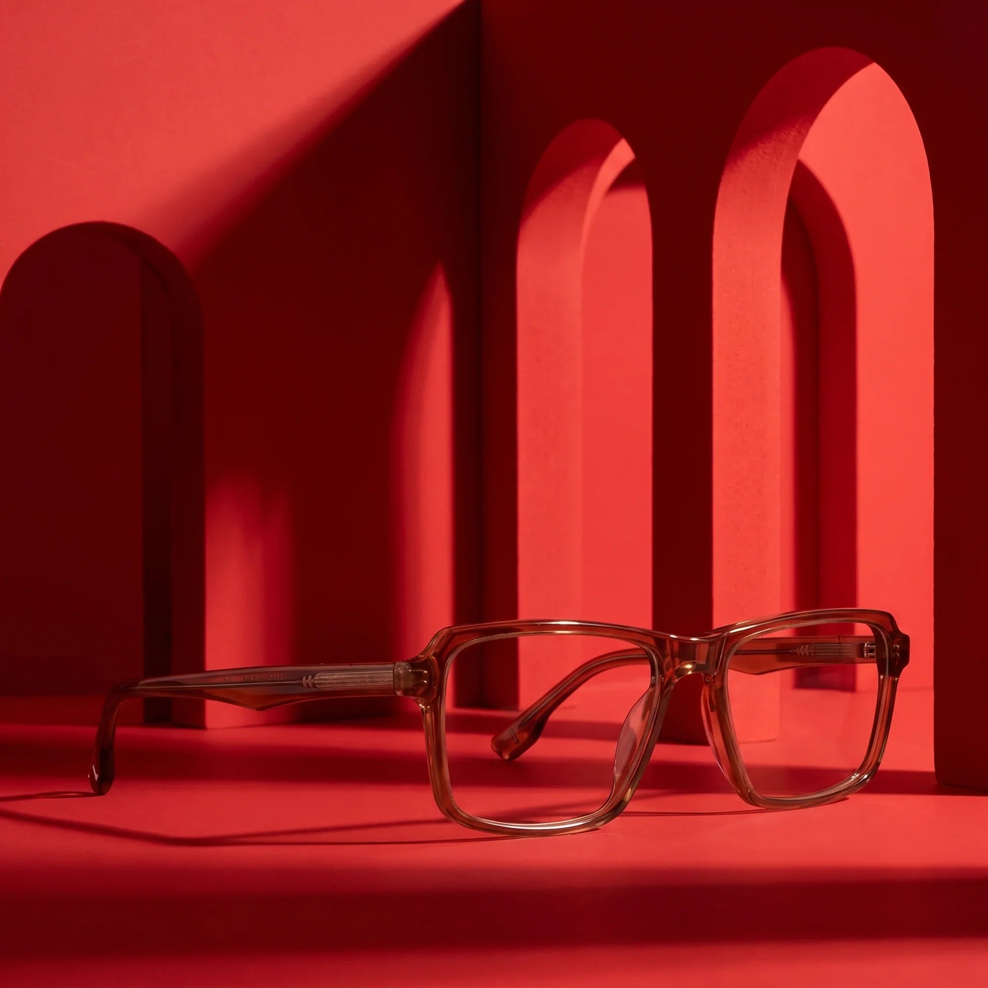 Anteojos Fiore 1038 en café – displayed on a vivid red podium among arches
