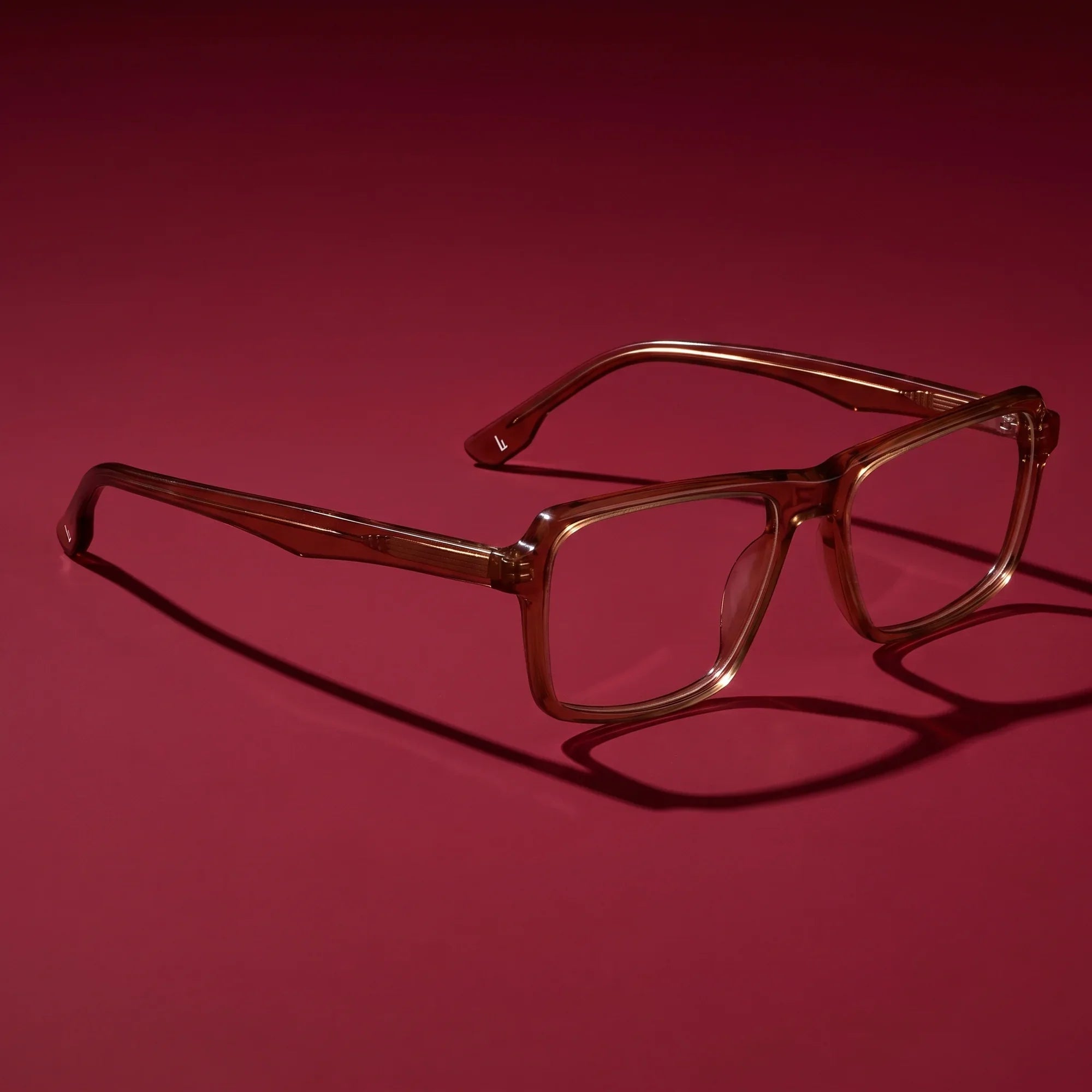 Anteojos Fiore 1038 en café – editorial still life on a saturated burgundy set
