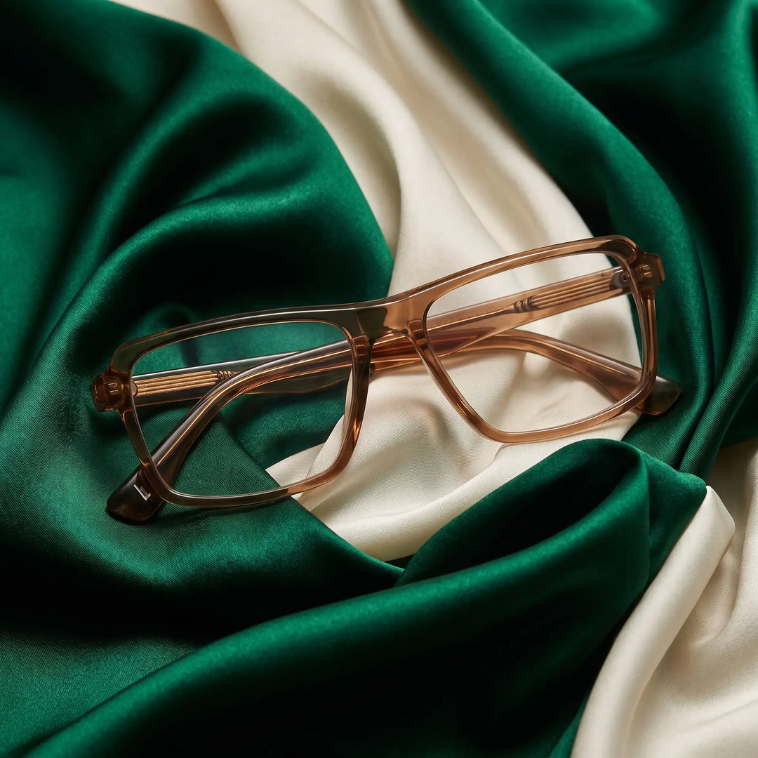 Anteojos Fiore 1038 en café – resting on draped emerald and ivory silk