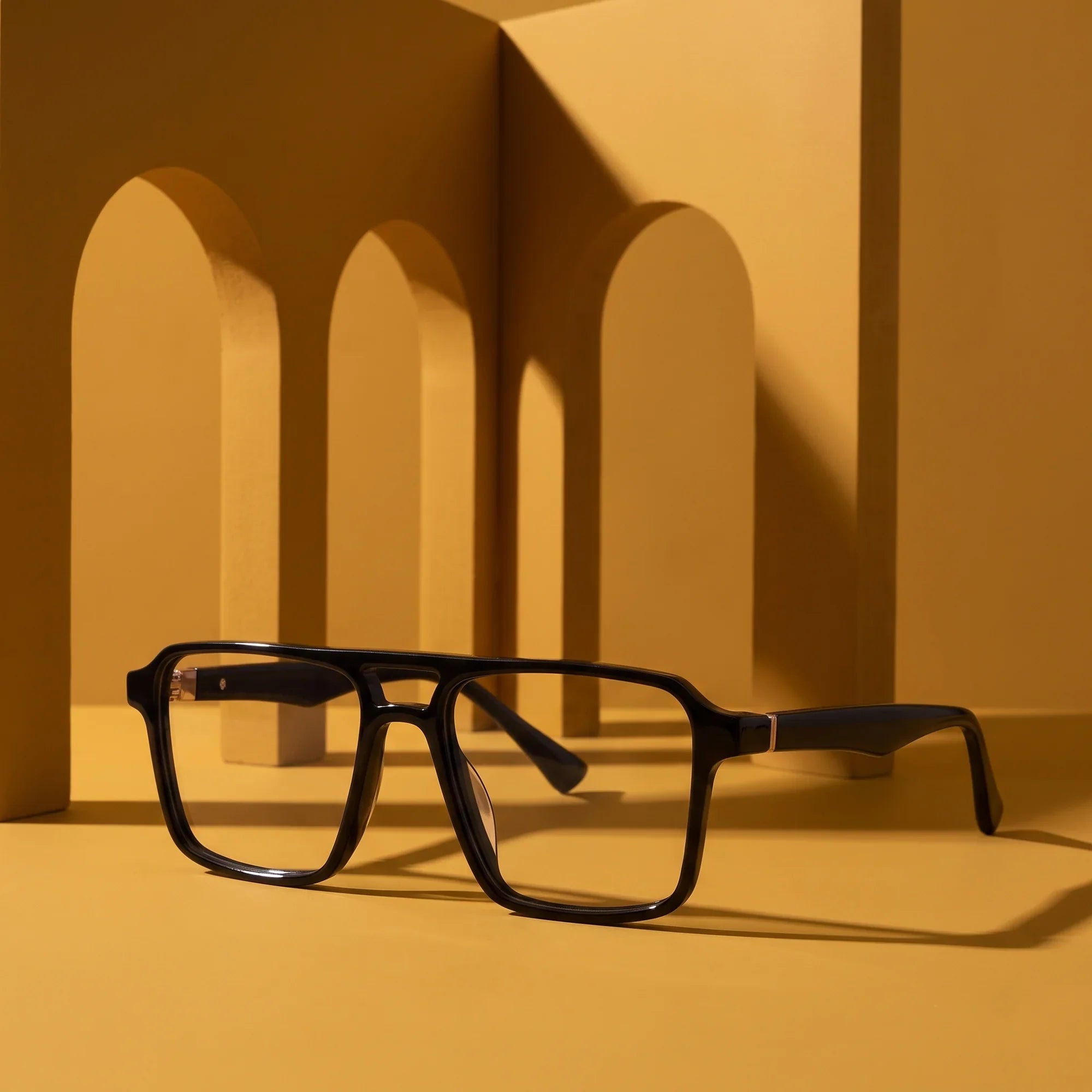 Anteojos Fiore 1039 en negro – displayed on a mustard ochre podium among arches