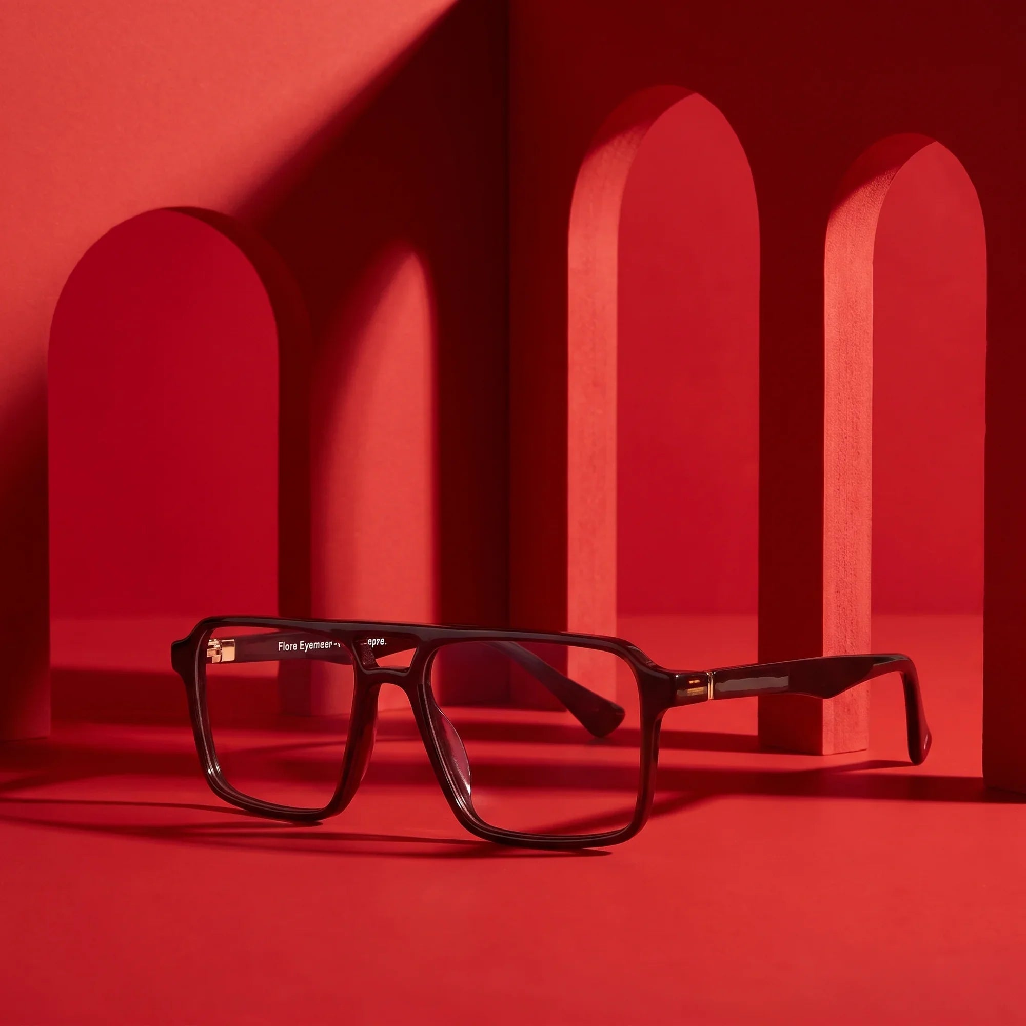 Anteojos Fiore 1039 en café – displayed on a vivid red podium among arches