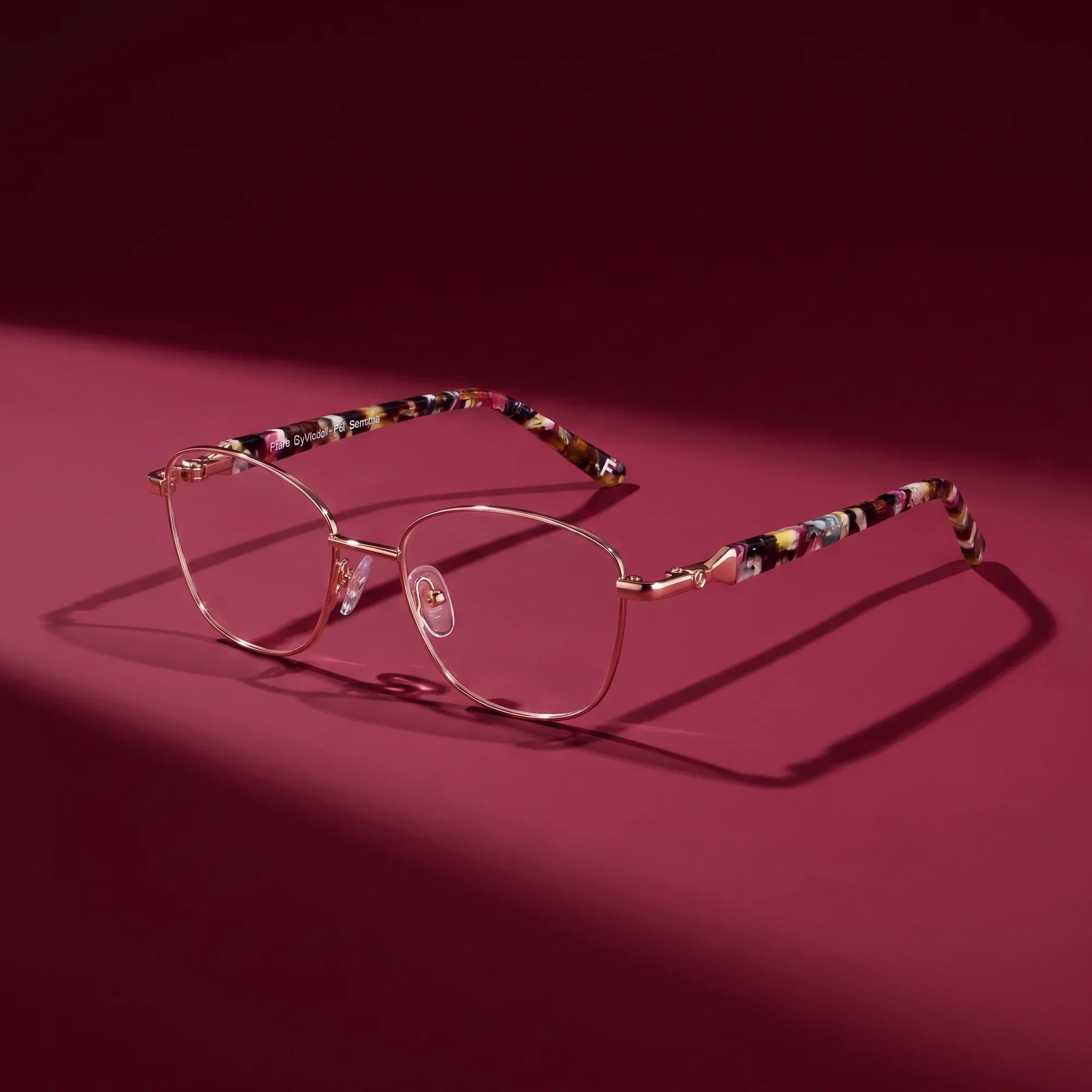 Anteojos Fiore 2208 en brown gold – editorial still life on a saturated burgundy set