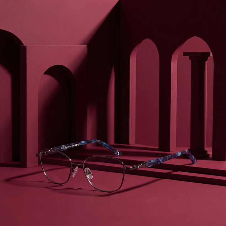 Anteojos Fiore 2208 en gunmetal azul – staged on a sculptural burgundy architecture set