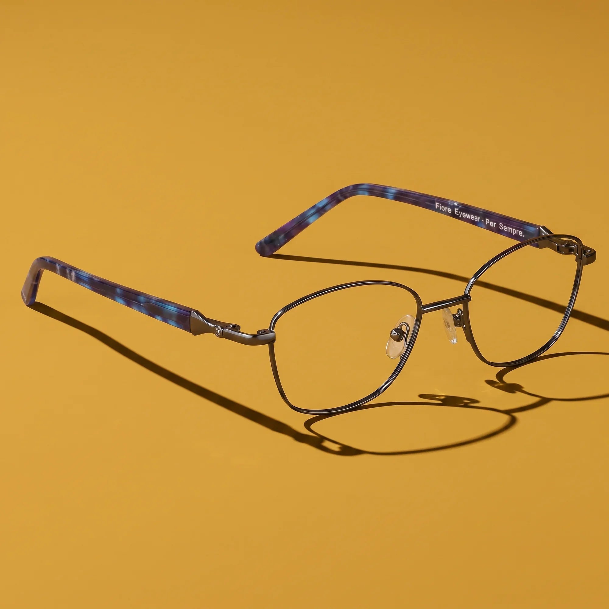 Anteojos Fiore 2208 en gun blue – hero still life against a deep mustard ochre backdrop