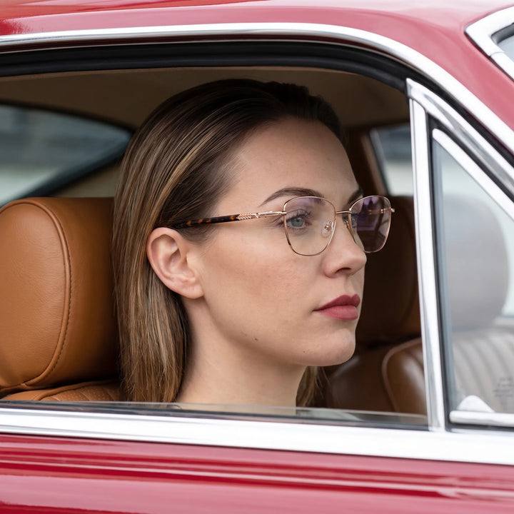 Anteojos Fiore 2210 en gold pink, en modelo – retrato de campaña, mirada a través de la ventana de un auto clásico rojo