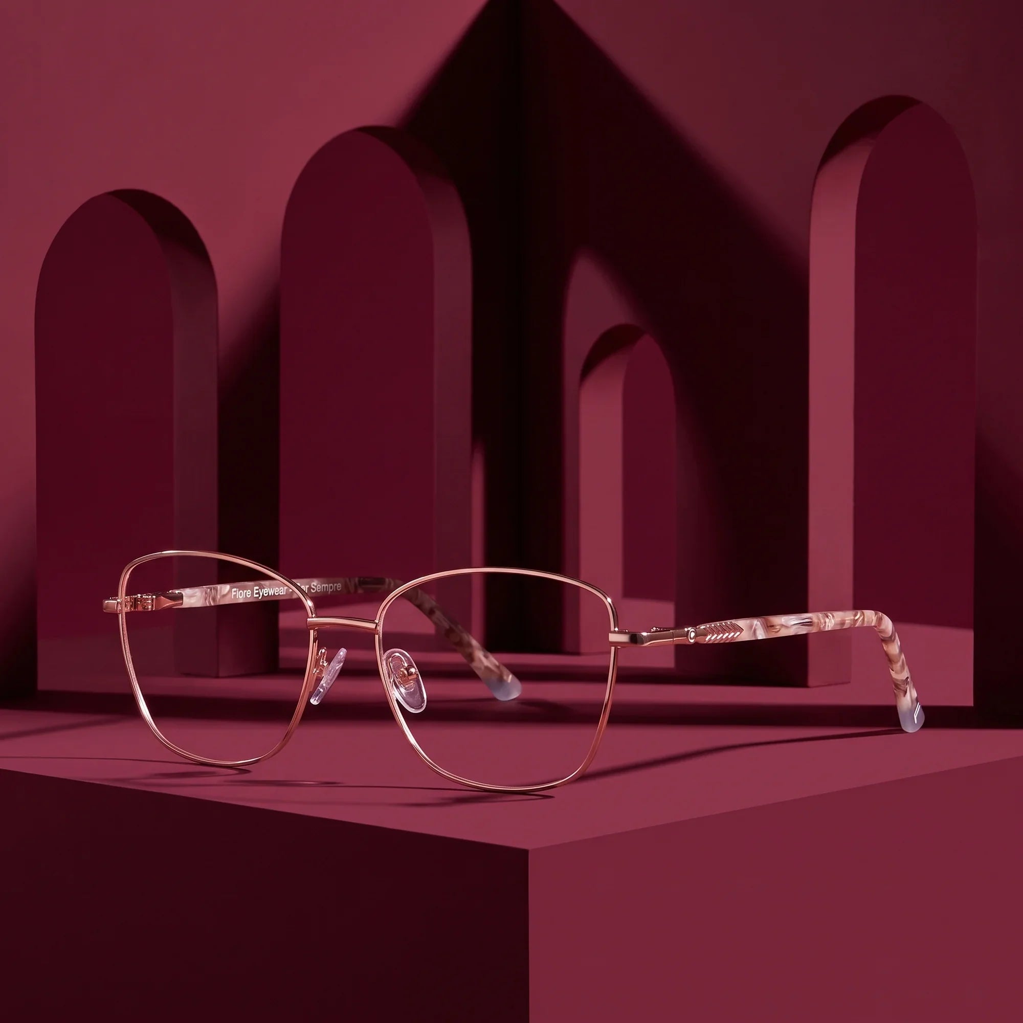 Anteojos Fiore 2210 en gold brown – displayed on a burgundy podium among arches