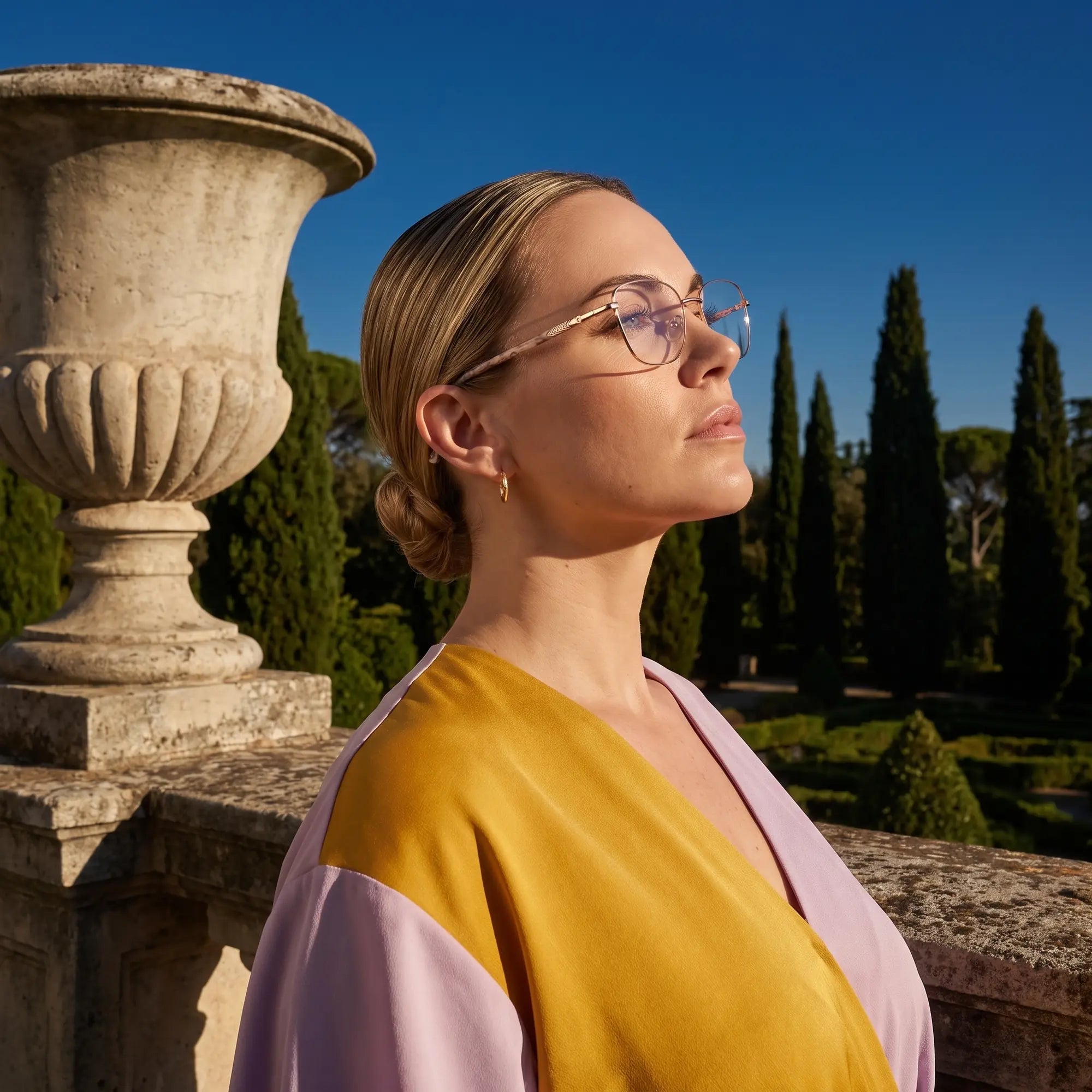 Anteojos Fiore 2210 en gold brown, en modelo – retrato de campaña, luz de atardecer sobre un jardín de cipreses