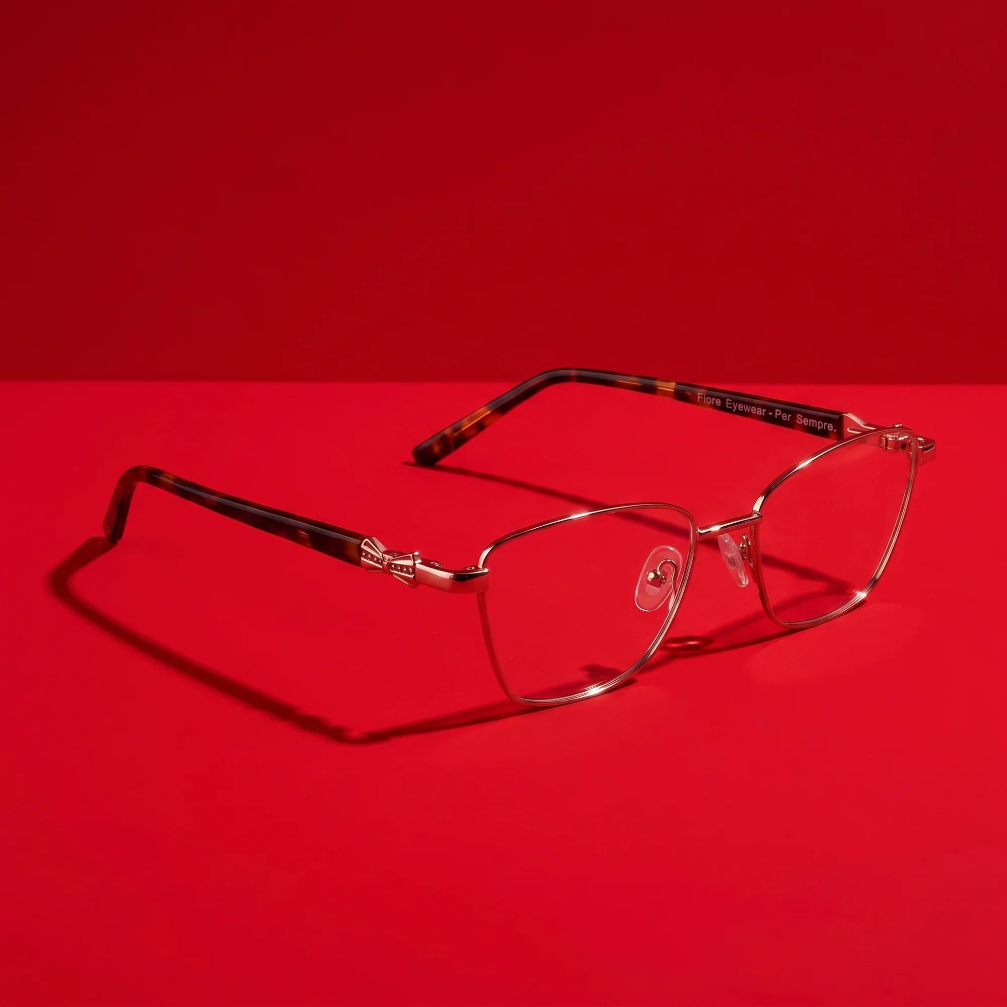 Anteojos Fiore 22115 en café – hero still life against a deep vivid red backdrop