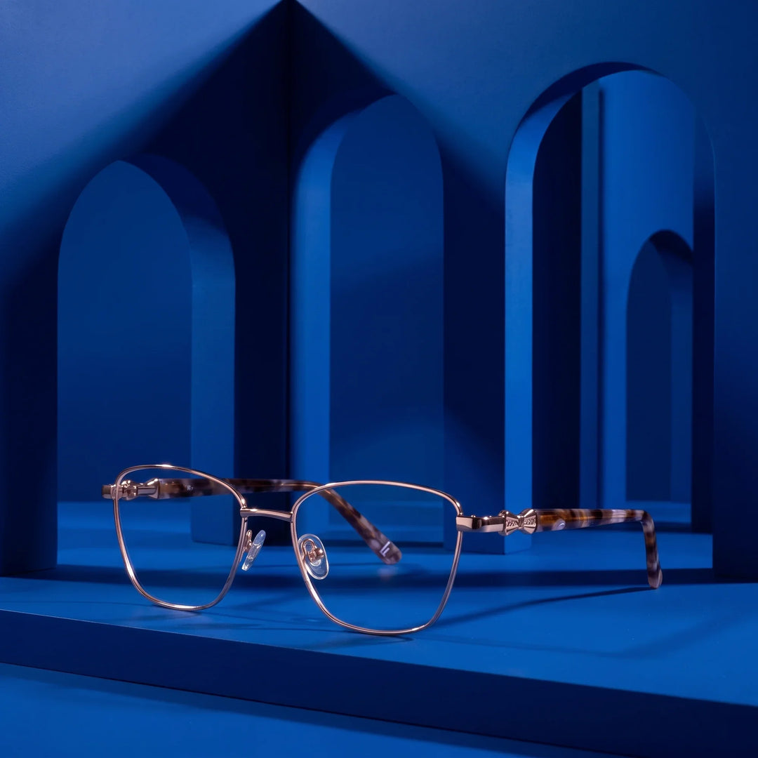 Anteojos Fiore 22115 en gold – displayed on a cobalt podium among arches