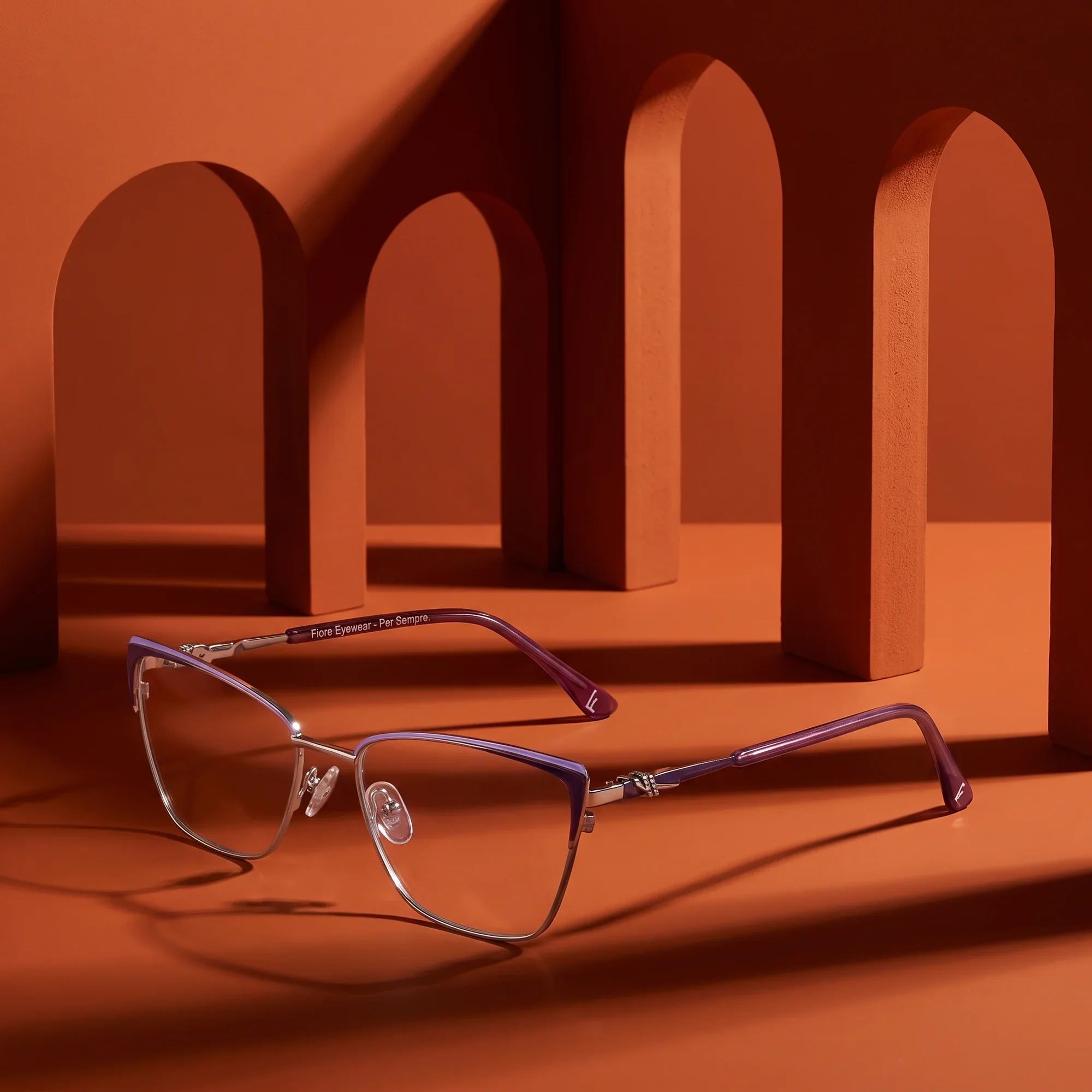 Anteojos Fiore 3839 en purple silver – displayed on a burnt orange podium among arches