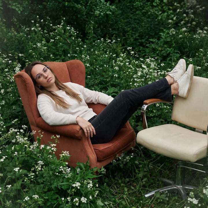 Anteojos Fiore 3839 en morado plateado, en modelo – retrato de campaña, lounging in an armchair in a wildflower meadow