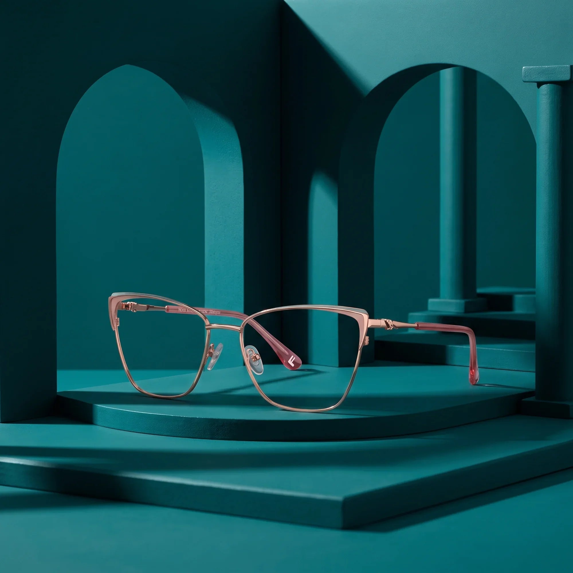 Anteojos Fiore 3839 en pink gold – displayed on a teal podium among arches
