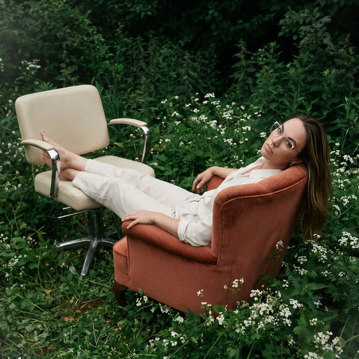 Anteojos Fiore 3839 en pink gold, en modelo – retrato de campaña, lounging in an armchair in a wildflower meadow